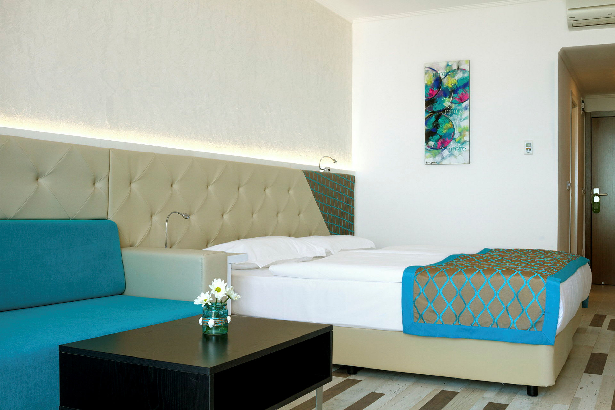 Et moderne hotellrom med en dobbeltseng, turkis sofa og veggkunst. (AI-generert tekst)