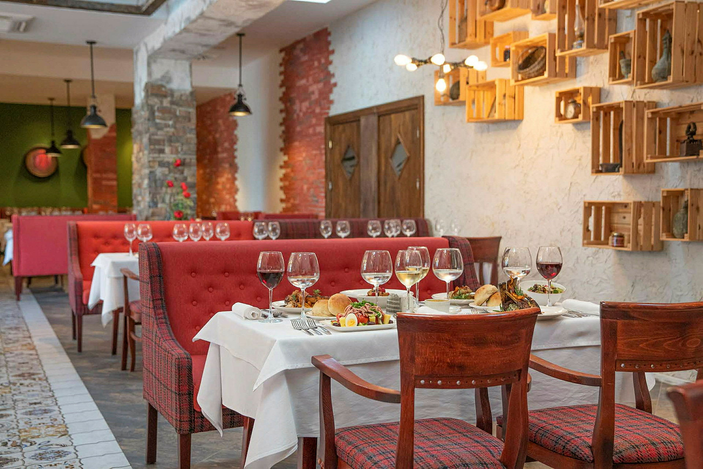 En restaurant med røde sofaer, tretstoler og dekkede bord med vinglass og matserveringer. (AI-generert tekst)