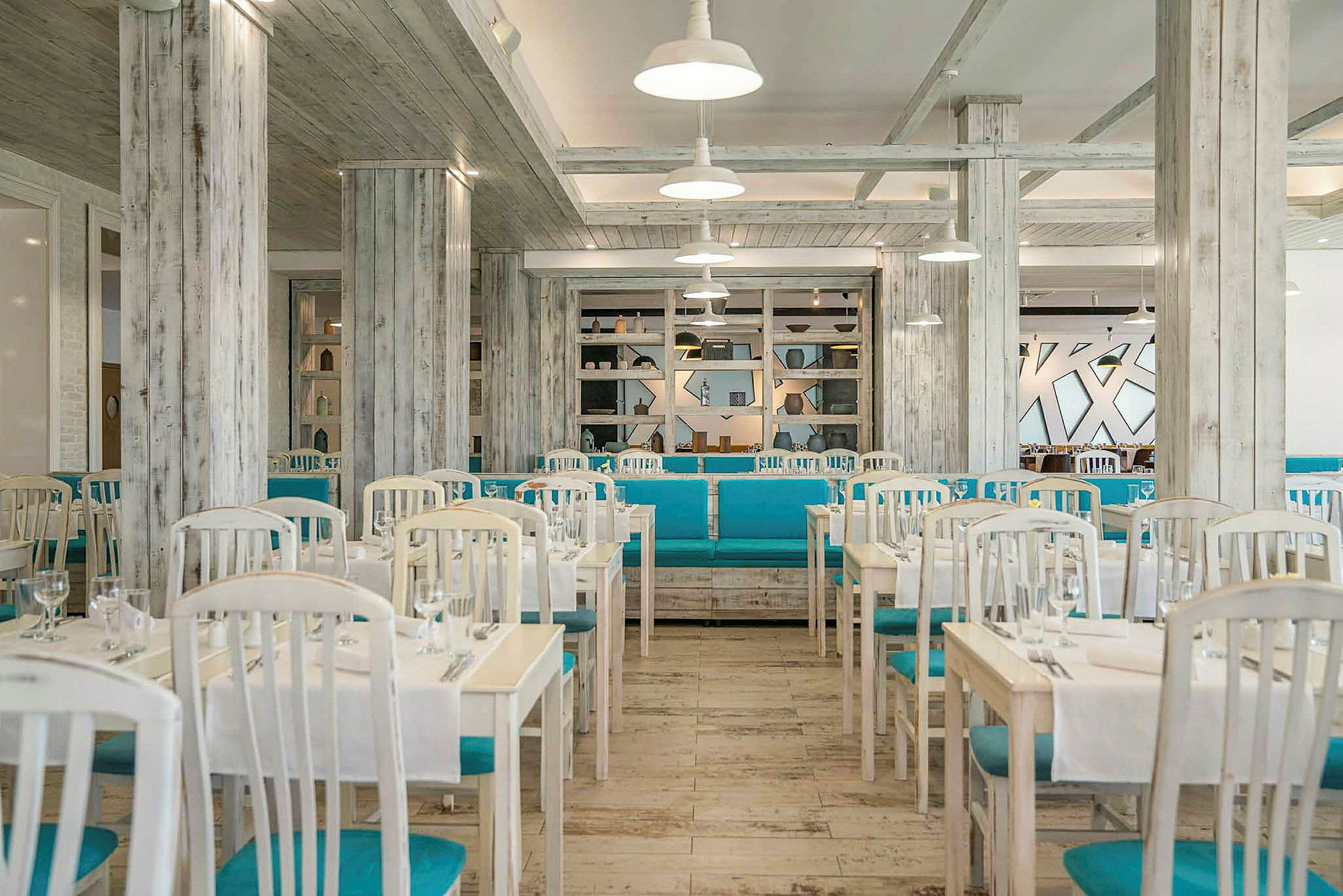 En lys restaurant med hvite bord, blå stoler og en stilren innredning. (AI-generert tekst)
