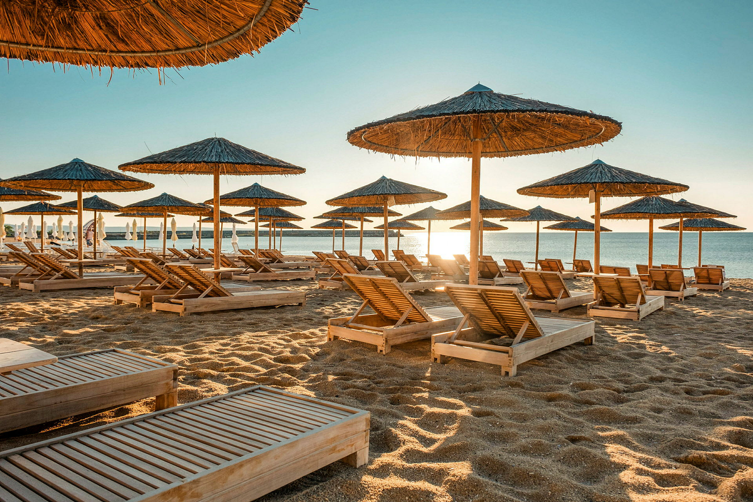 Strand med solsenger og parasoller av halm ved vannet. (AI-generert tekst)