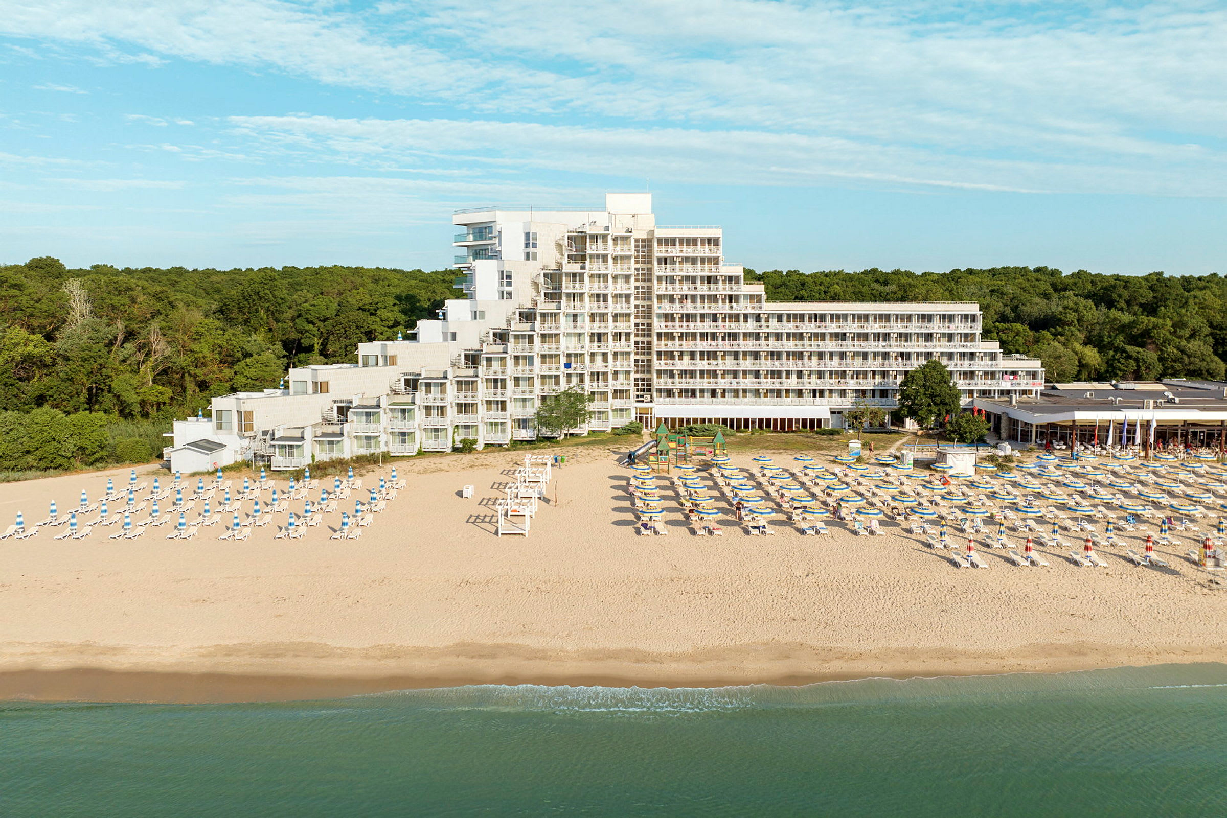 En strand med solsenger og parasoller foran et hotell ved kysten. (AI-generert tekst)
