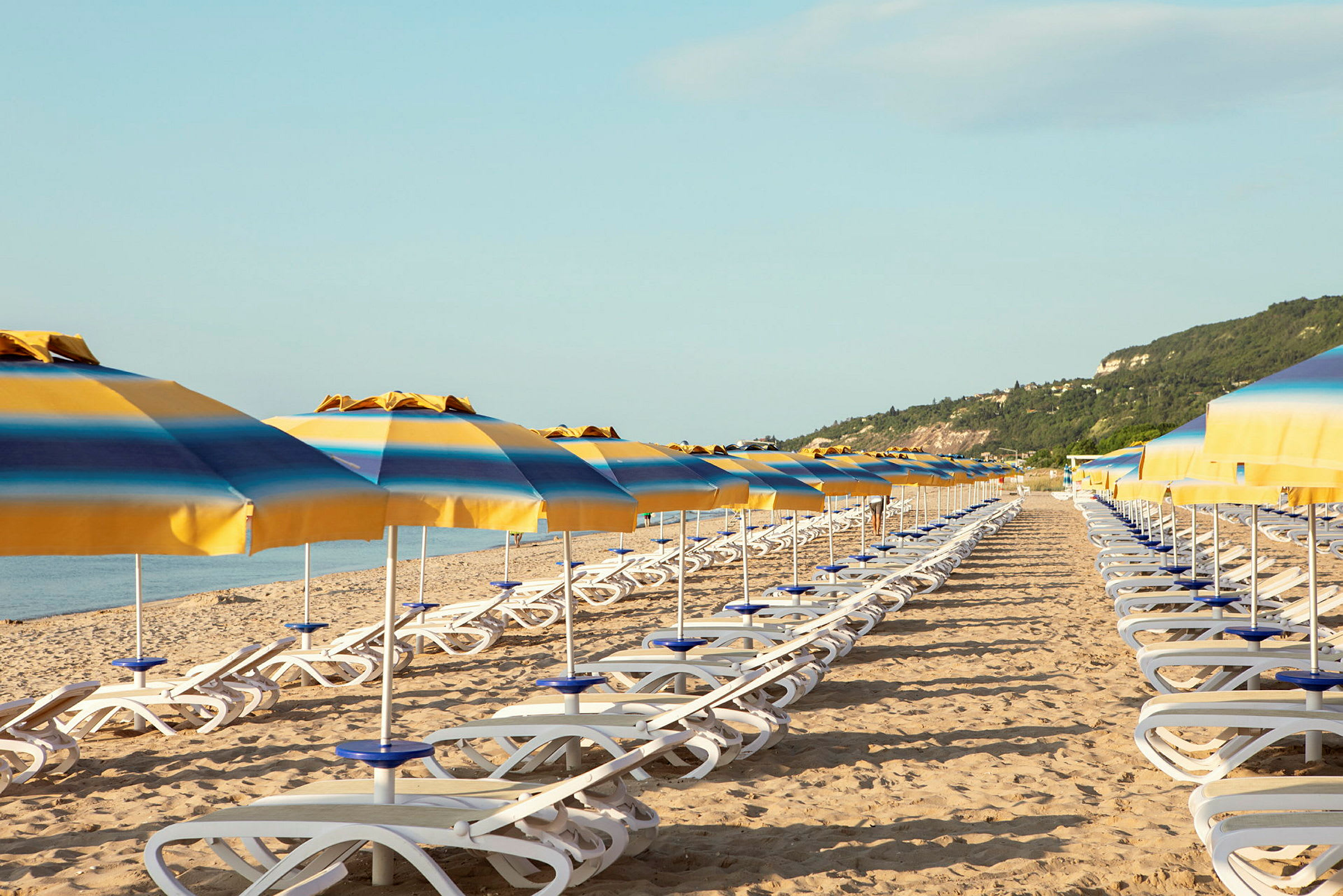 Flere solsenger med gule og blå parasoller på en sandstrand. (AI-generert tekst)