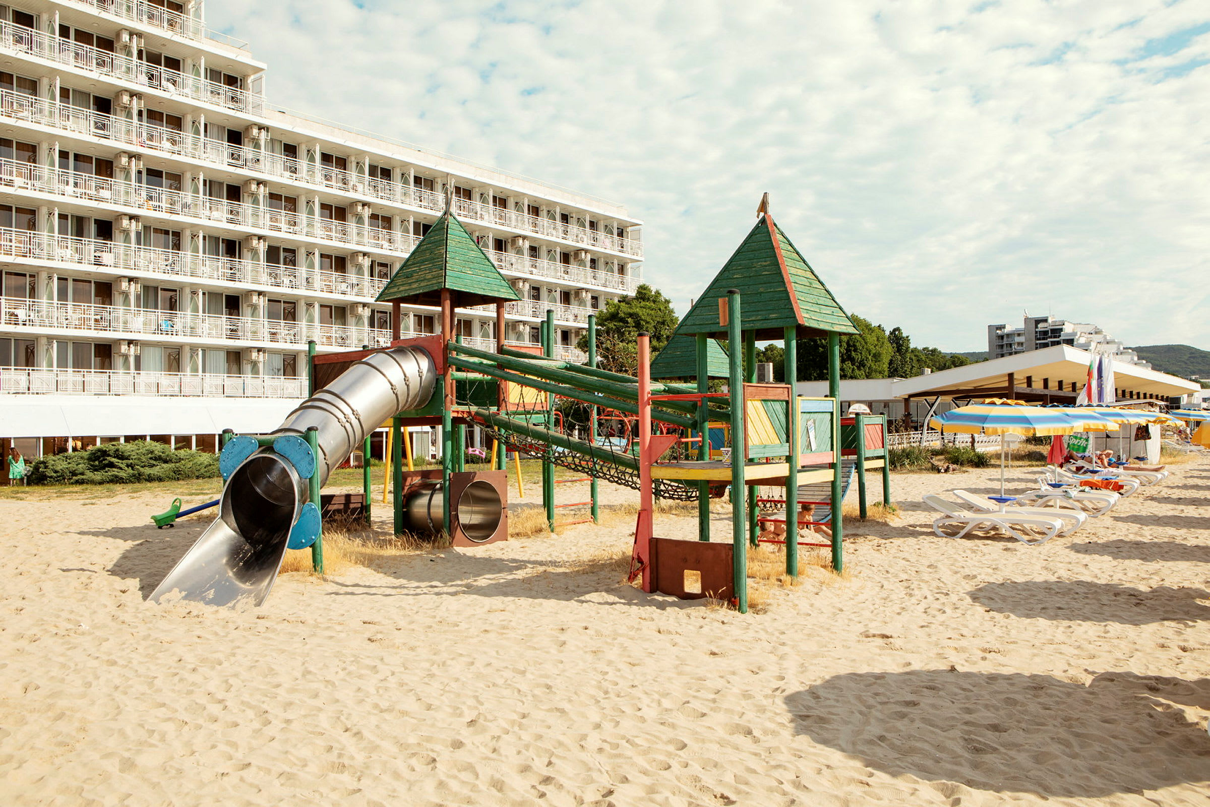Lekeplass med sklir på sandstrand foran hotell. (AI-generert tekst)