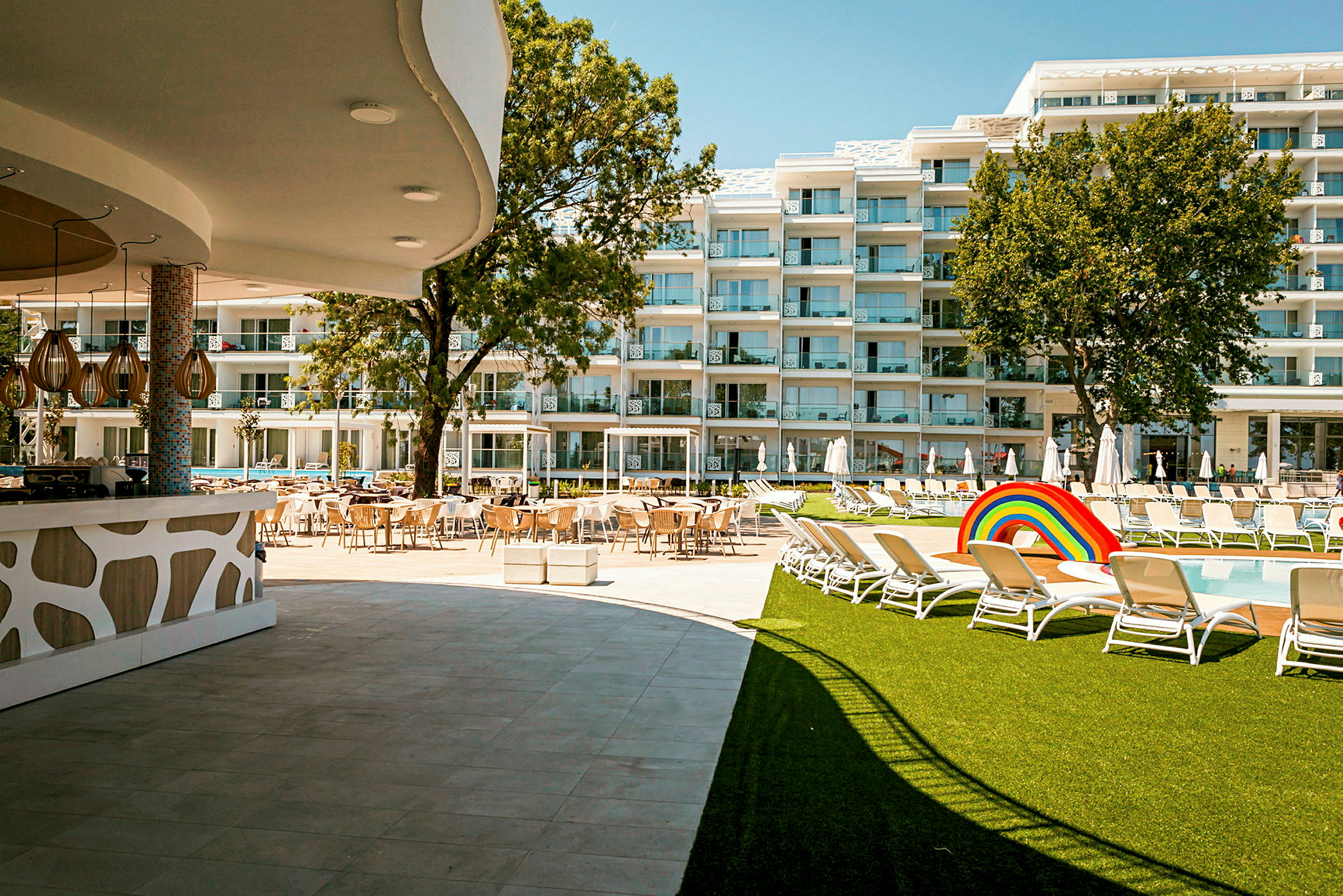 Hotellområde med basseng, solsenger, plen og bygninger i bakgrunnen. (AI-generert tekst)