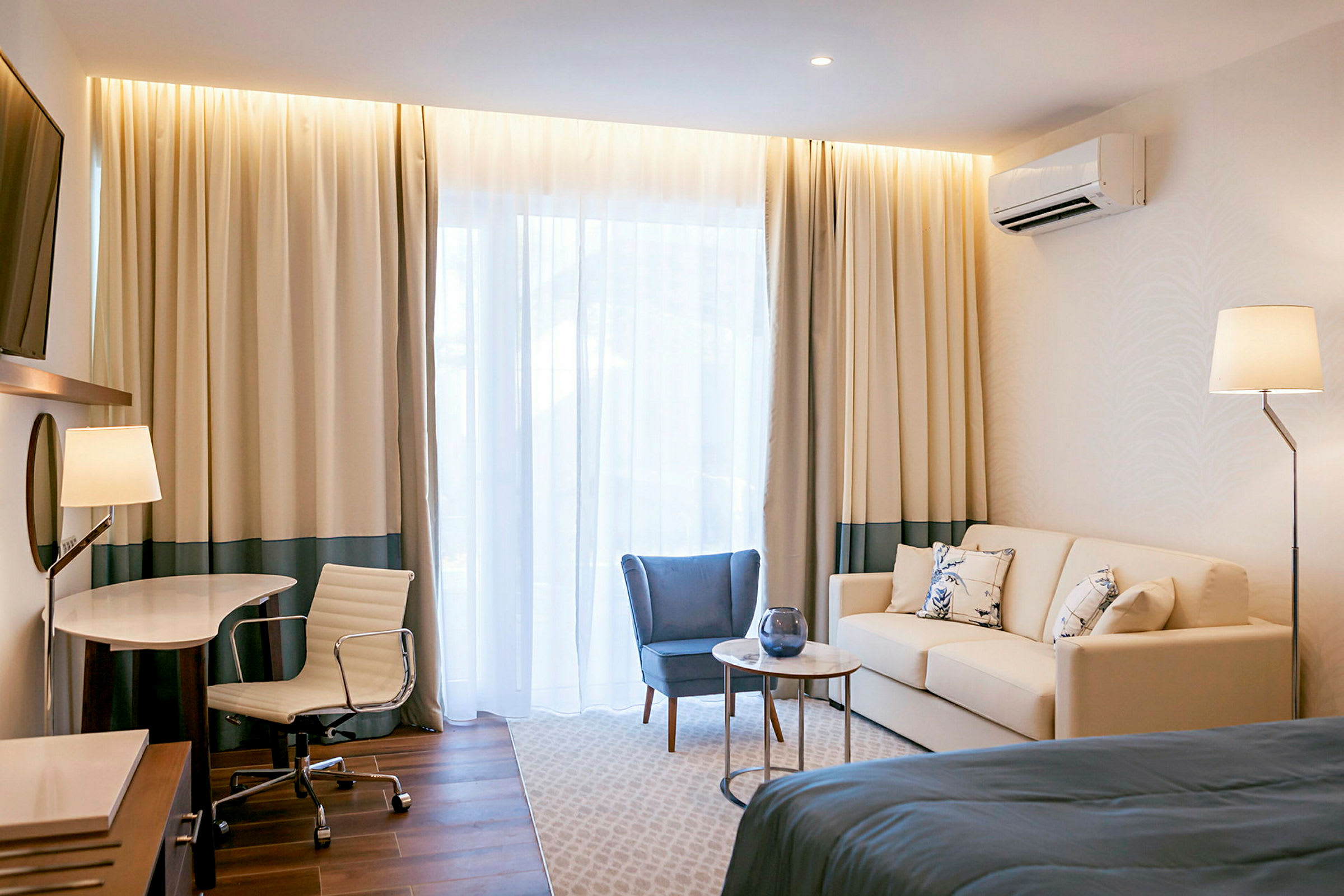 Moderne innredet hotellrom med sofa, lenestol, skrivebord og en stor seng. (AI-generert tekst)