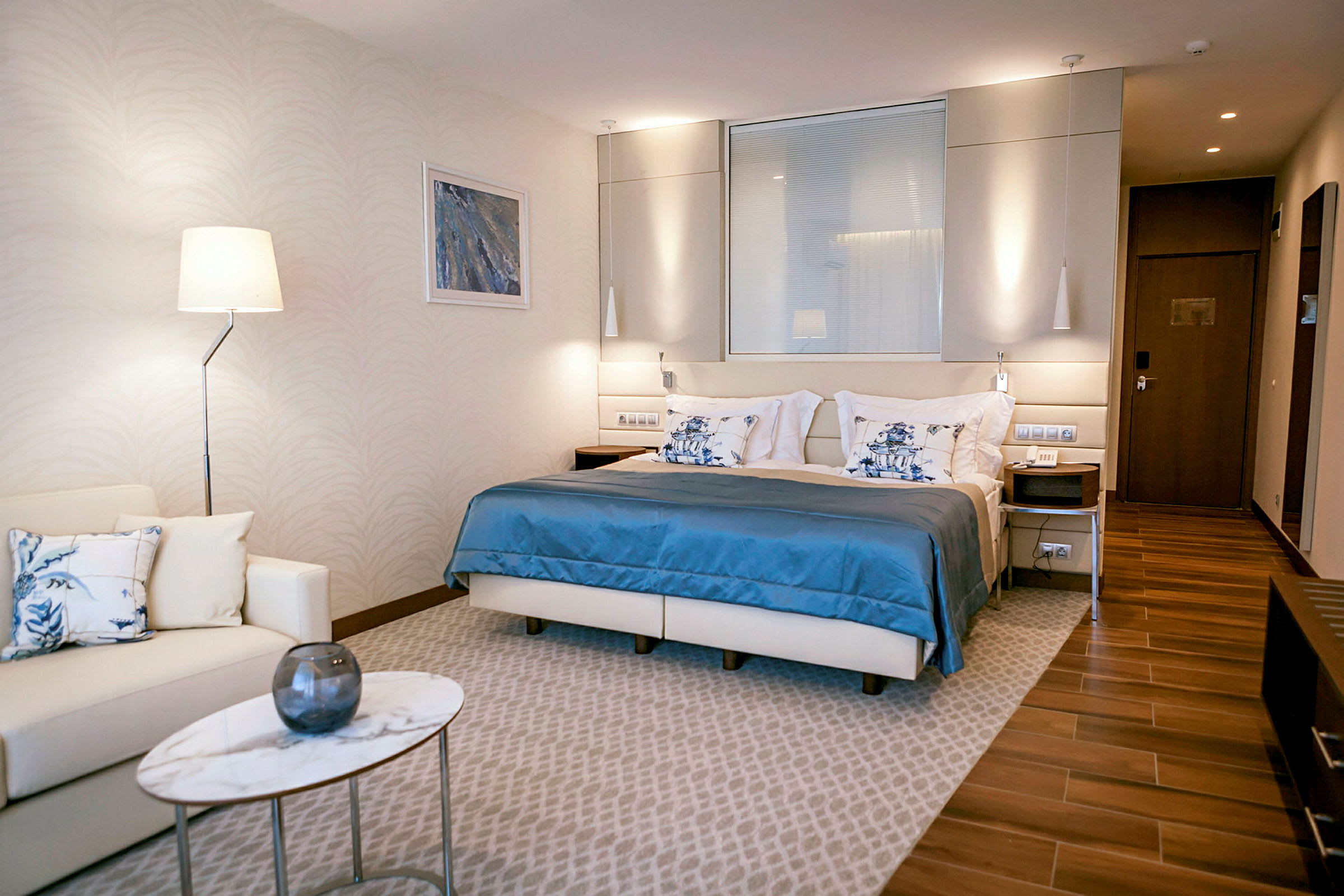 Et moderne hotellrom med en dobbeltseng, en sittegruppe og et lite marmorbord. (AI-generert tekst)