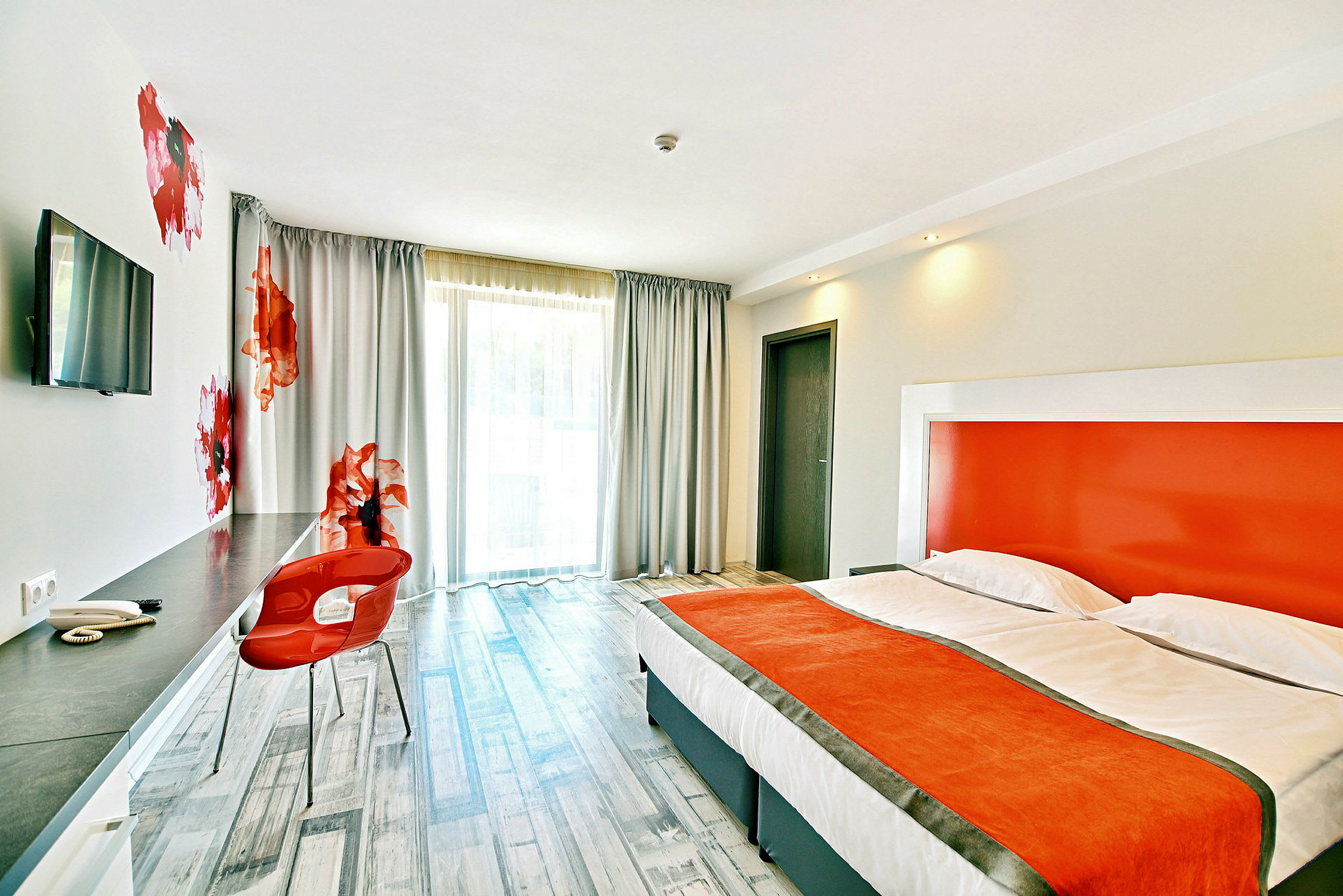 Moderne hotellrom med oransje detaljer, komfortabel seng og skrivebordsområde. (AI-generert tekst)