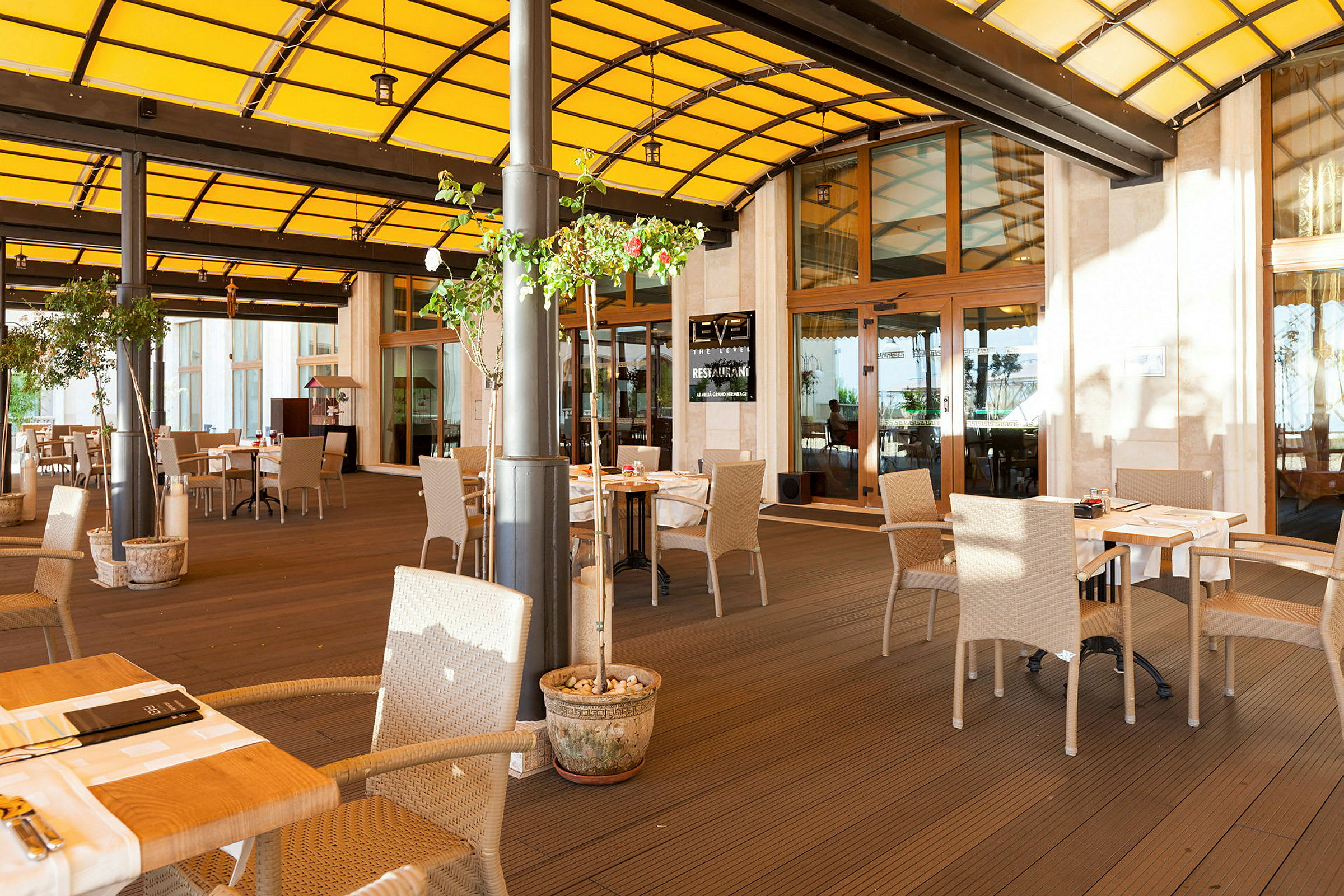 En utendørs terrasse med sitteplasser og bord under et gult tak. (AI-generert tekst)