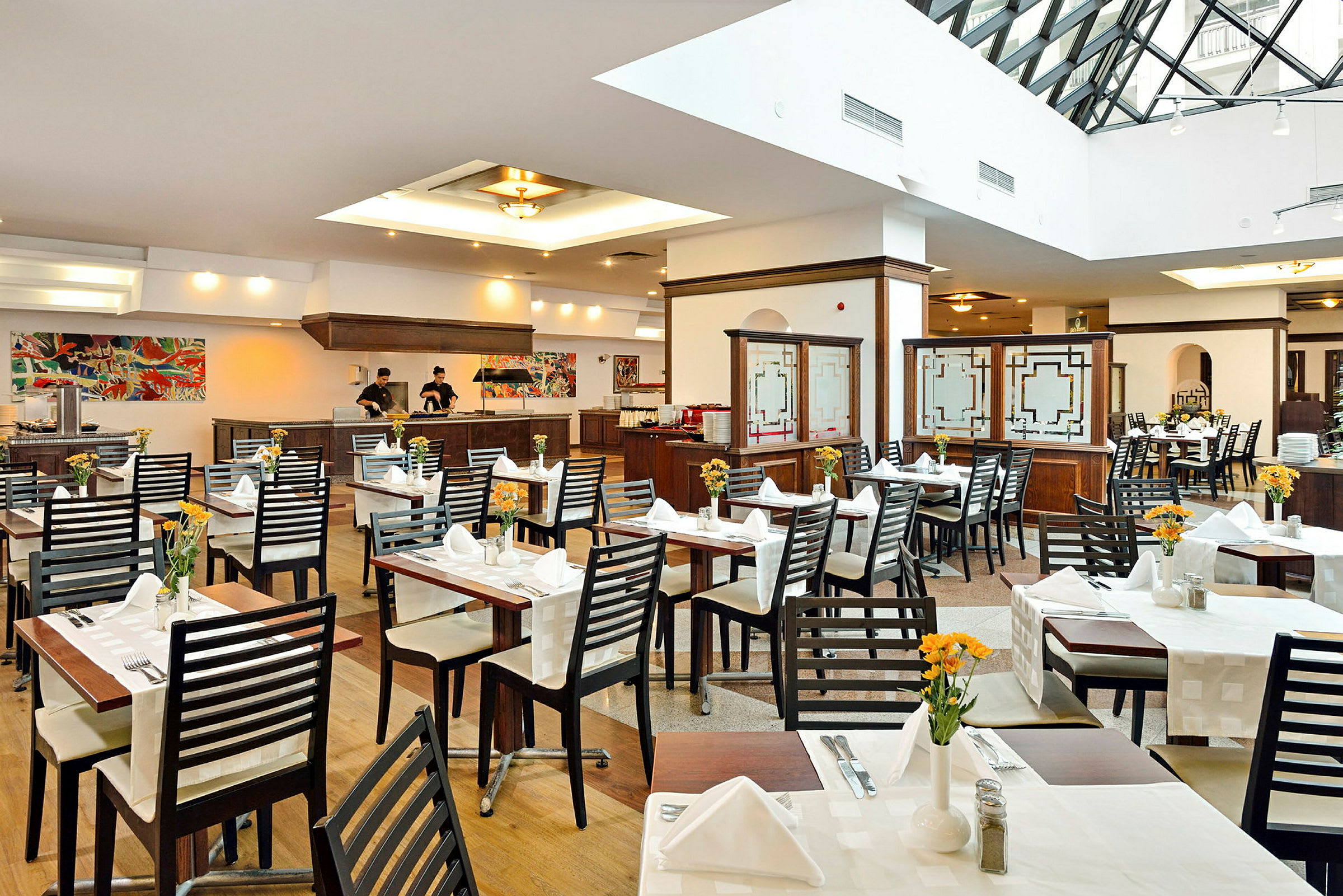 Interiør av en restaurant med bord satt opp og dekket, samt personale ved serveringsdisken. (AI-generert tekst)