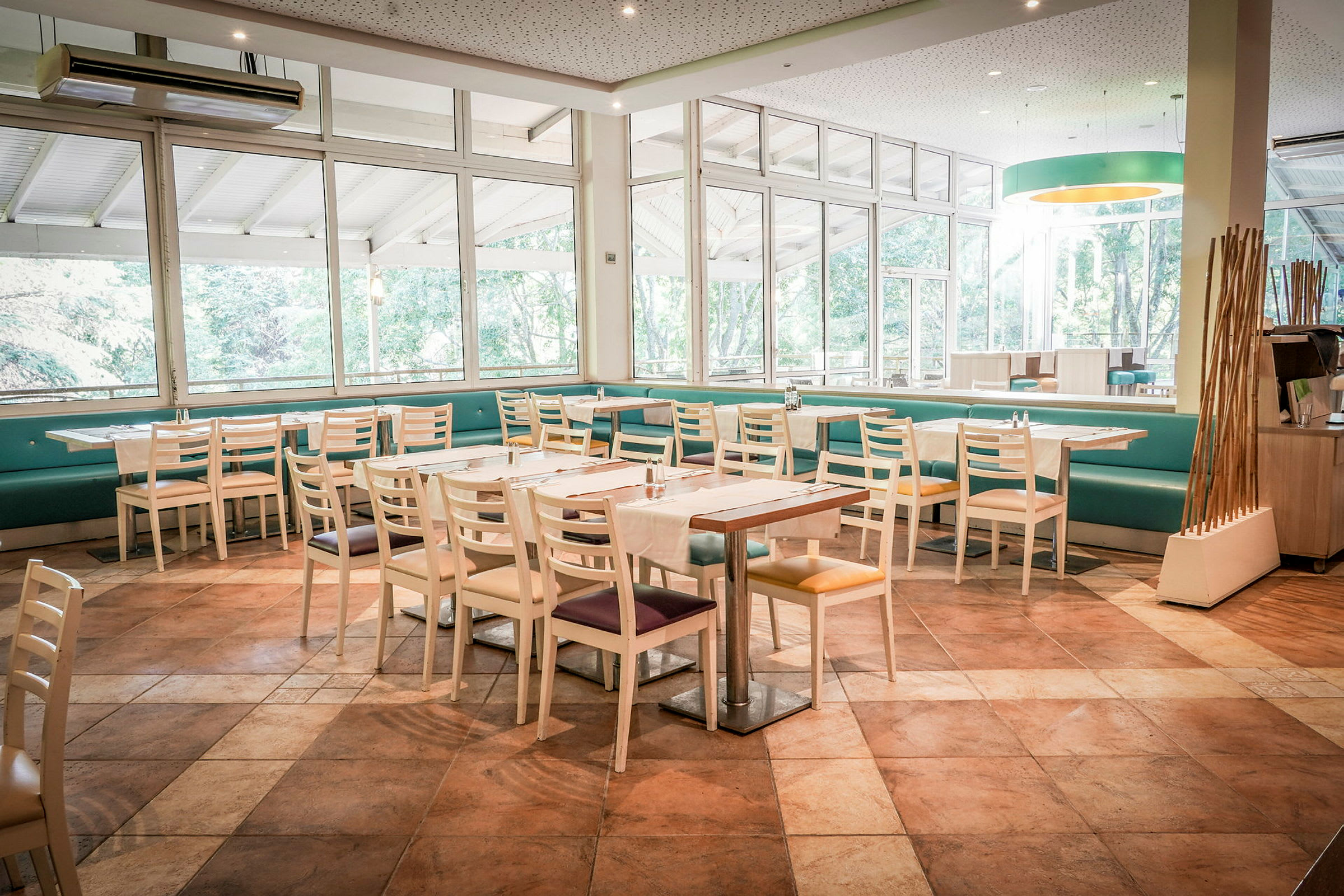Et lyst restaurantområde med bord og stoler samt store vinduer som vender mot grøntområder. (AI-generert tekst)