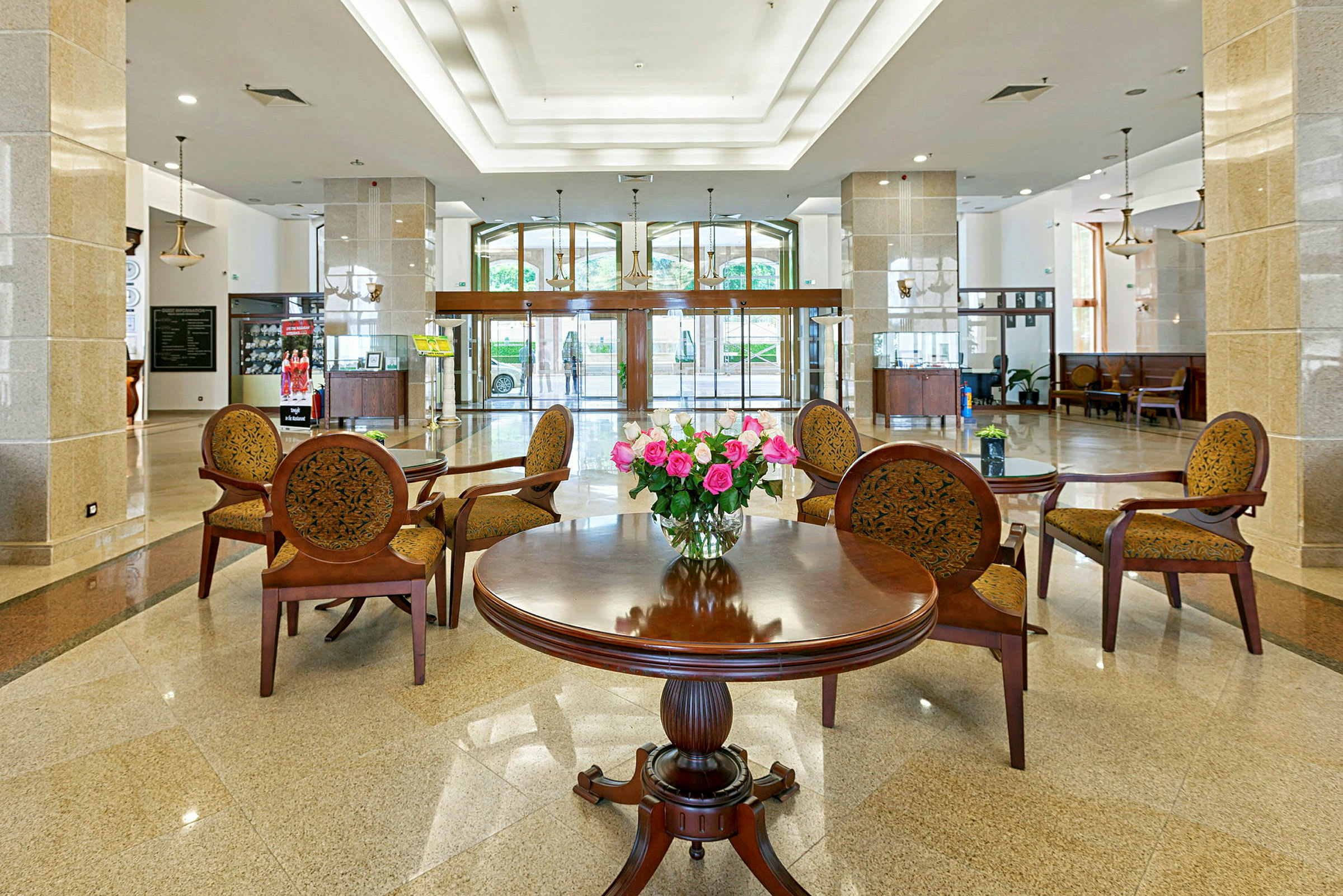 Hotellobby med bord og stoler rundt en blomsterbukett. (AI-generert tekst)