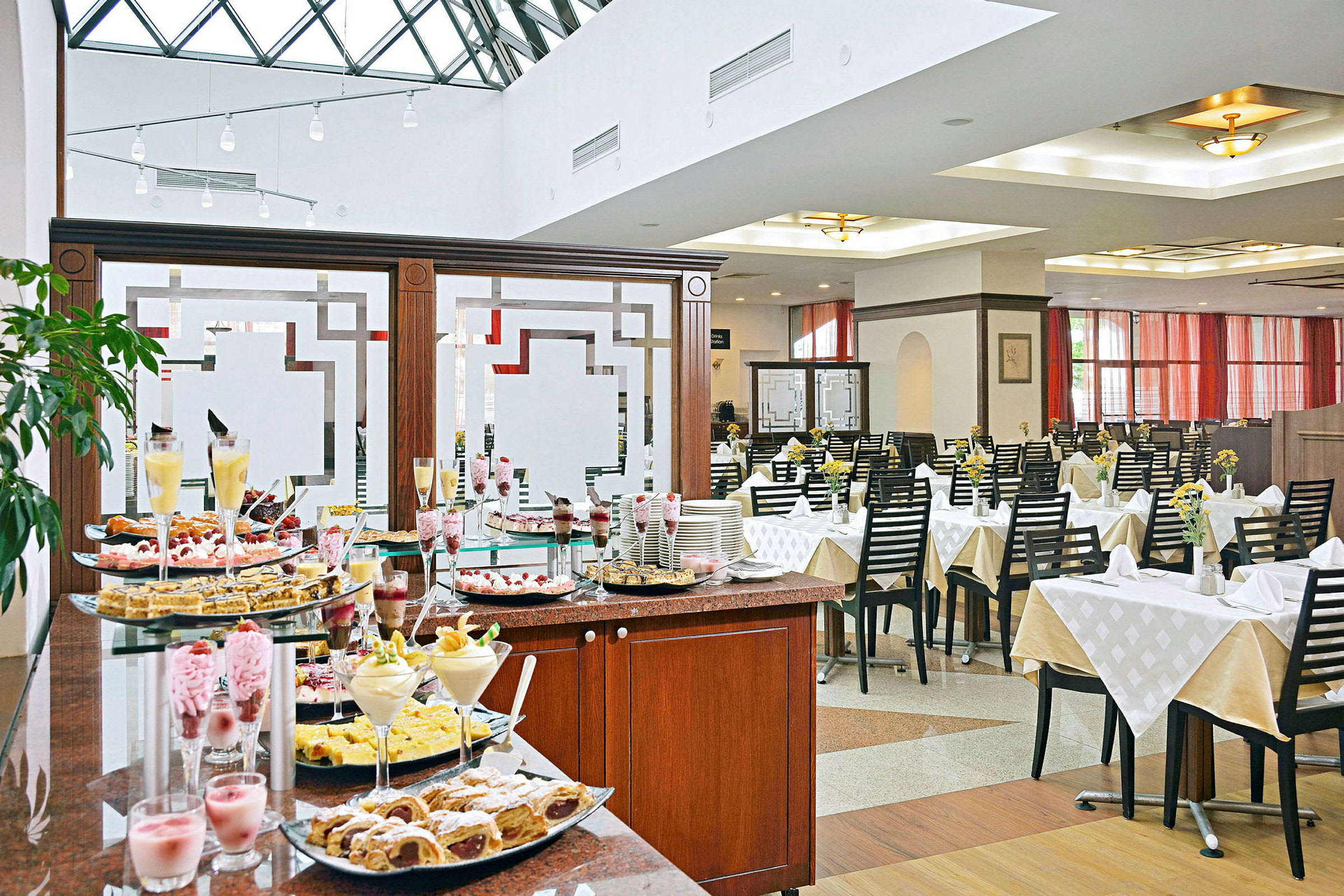 Buffetbord med desserter i en lys restaurant med dekkede bord. (AI-generert tekst)