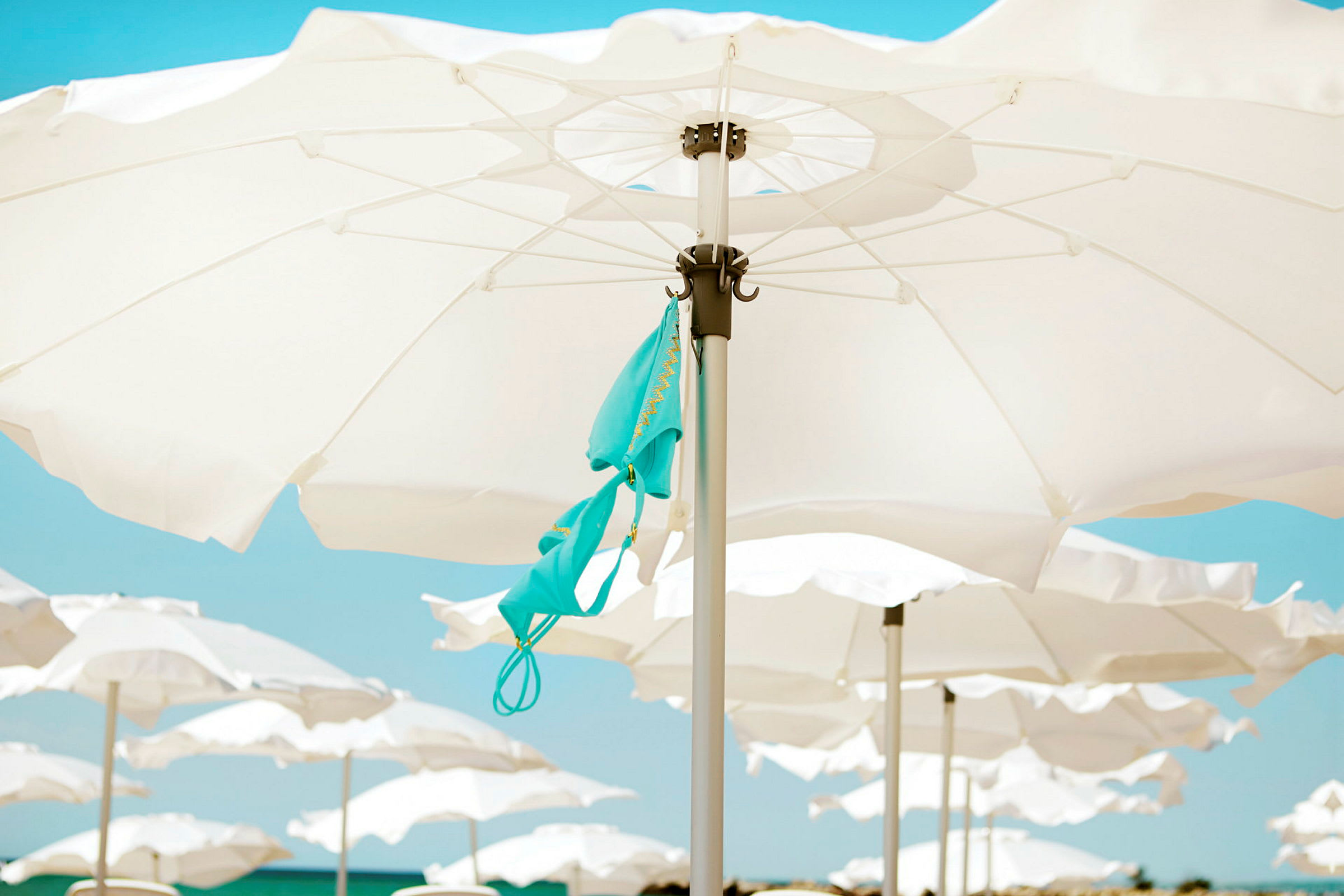 Parasoller på en strand med en turkis bikinioverdel hengende fra en av parasollene. (AI-generert tekst)