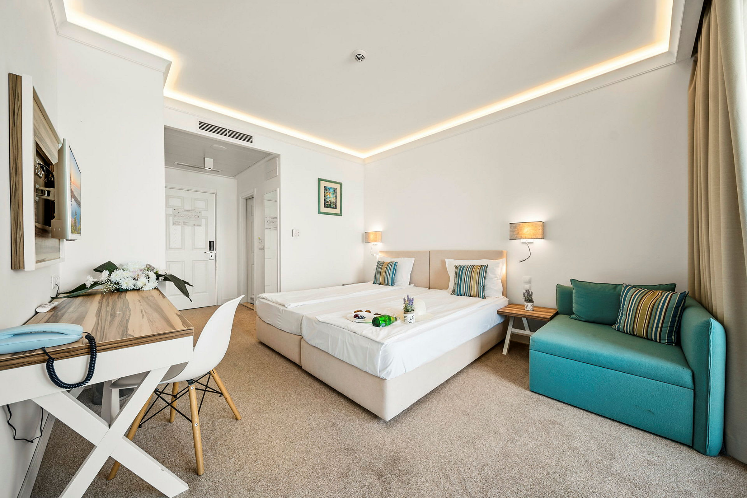 Et hotellrom med to enkeltsenger, et skrivebord og en grønn sofa. (AI-generert tekst)