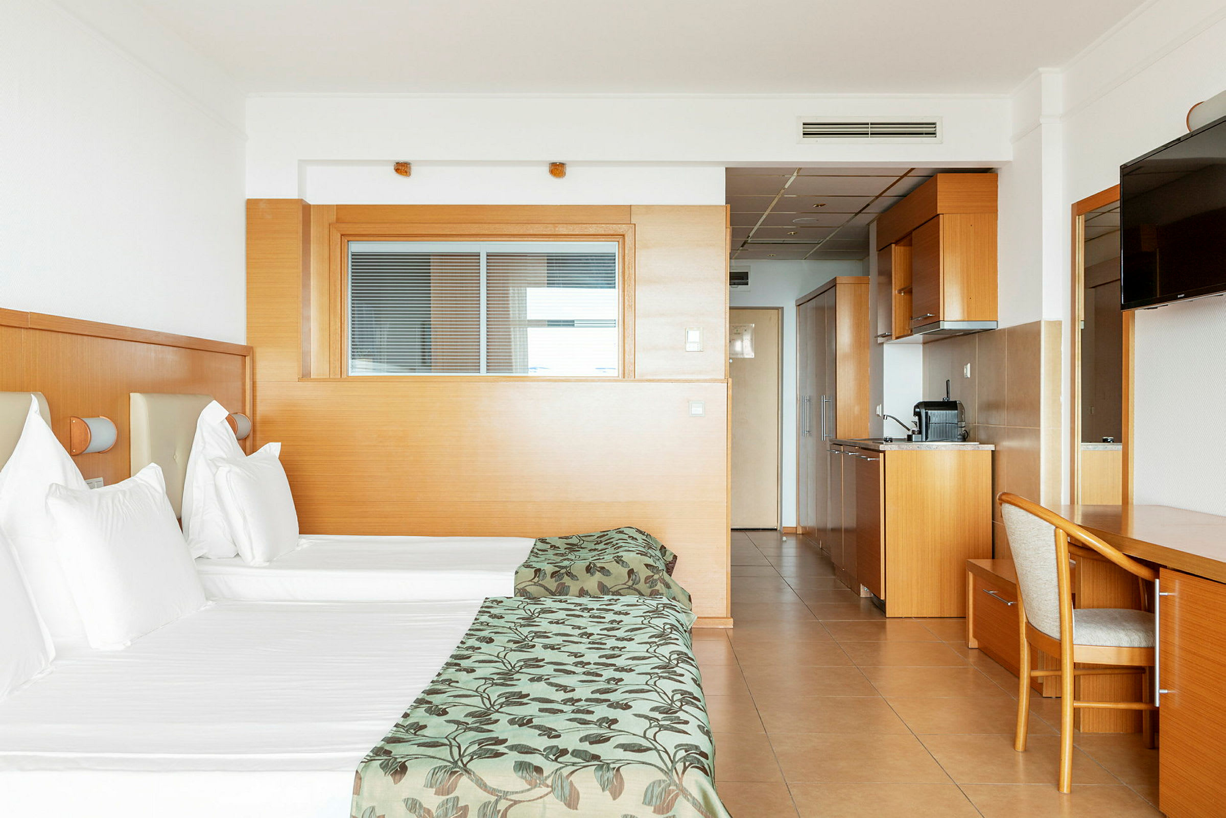 Hotellrom med to enkeltsenger, kjøkkenkrok og skrivebord. (AI-generert tekst)