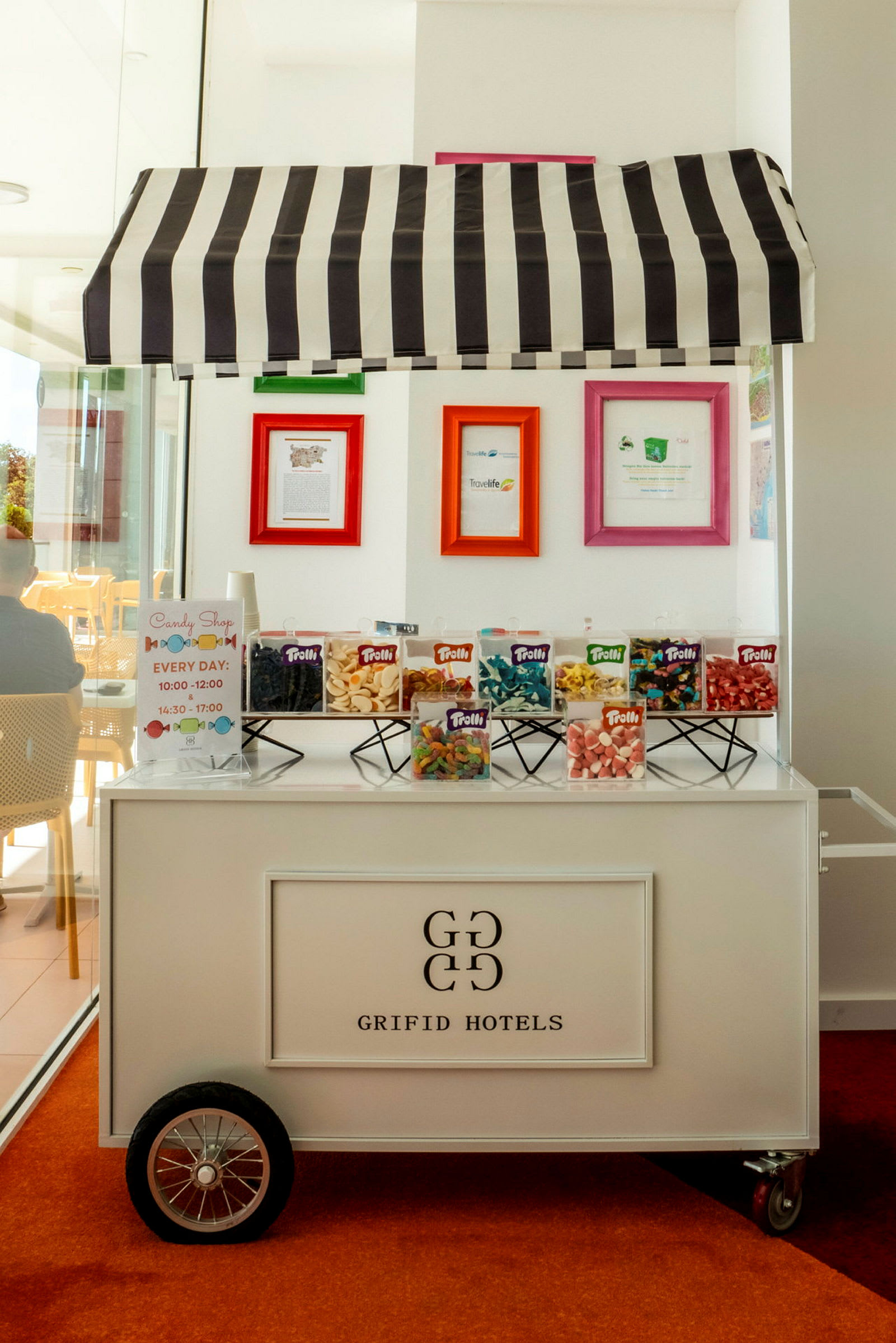En godterikiosk merket 'Grifid Hotels' med en stripet markise, der forskjellige typer godteri er utstilt. (AI-generert tekst)