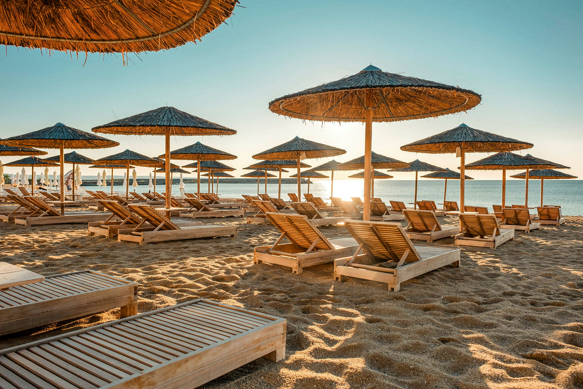 Strand med solsenger og parasoller i tre. (AI-generert tekst)