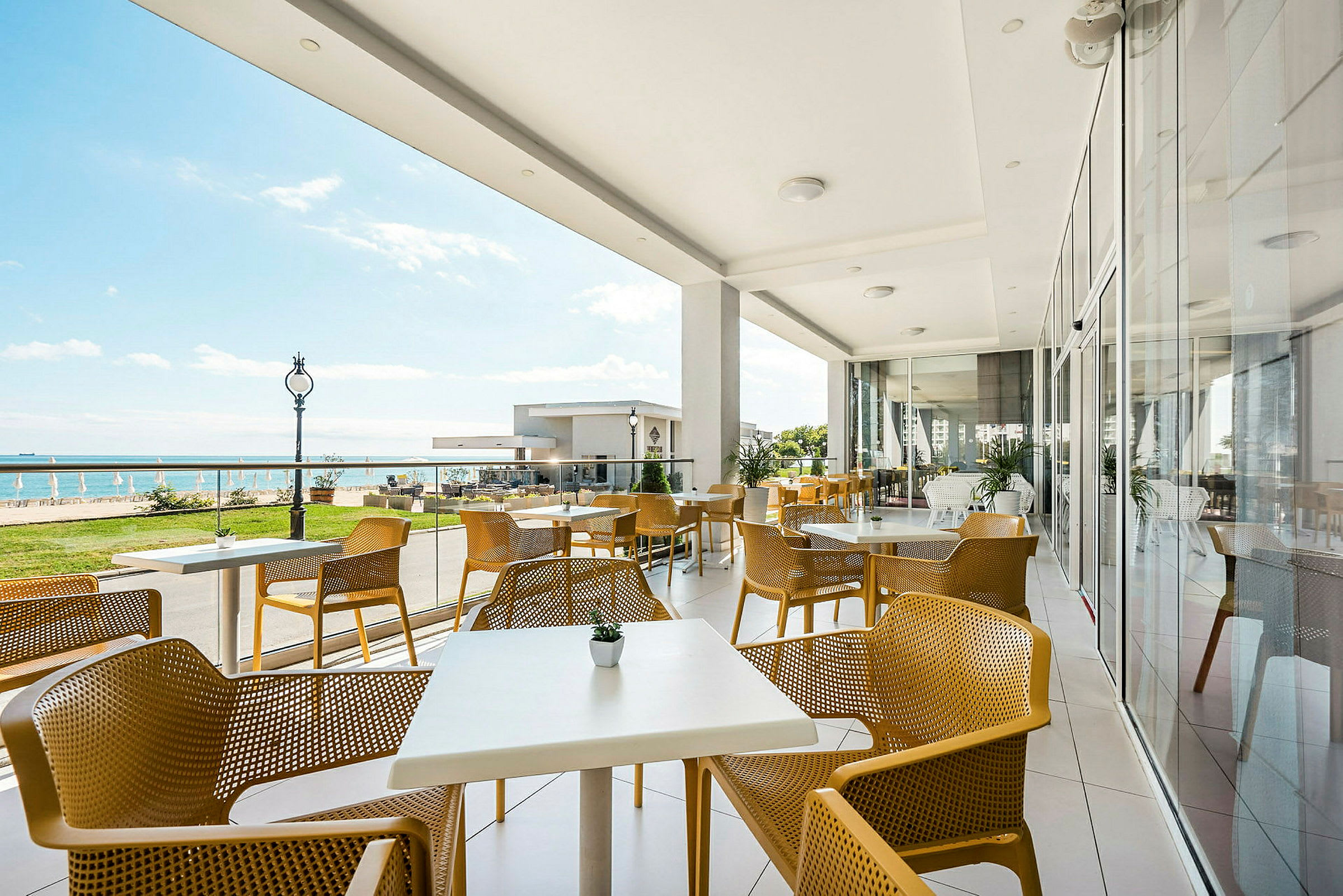En uteterrasse med gule stoler og hvite bord ved havet. (AI-generert tekst)