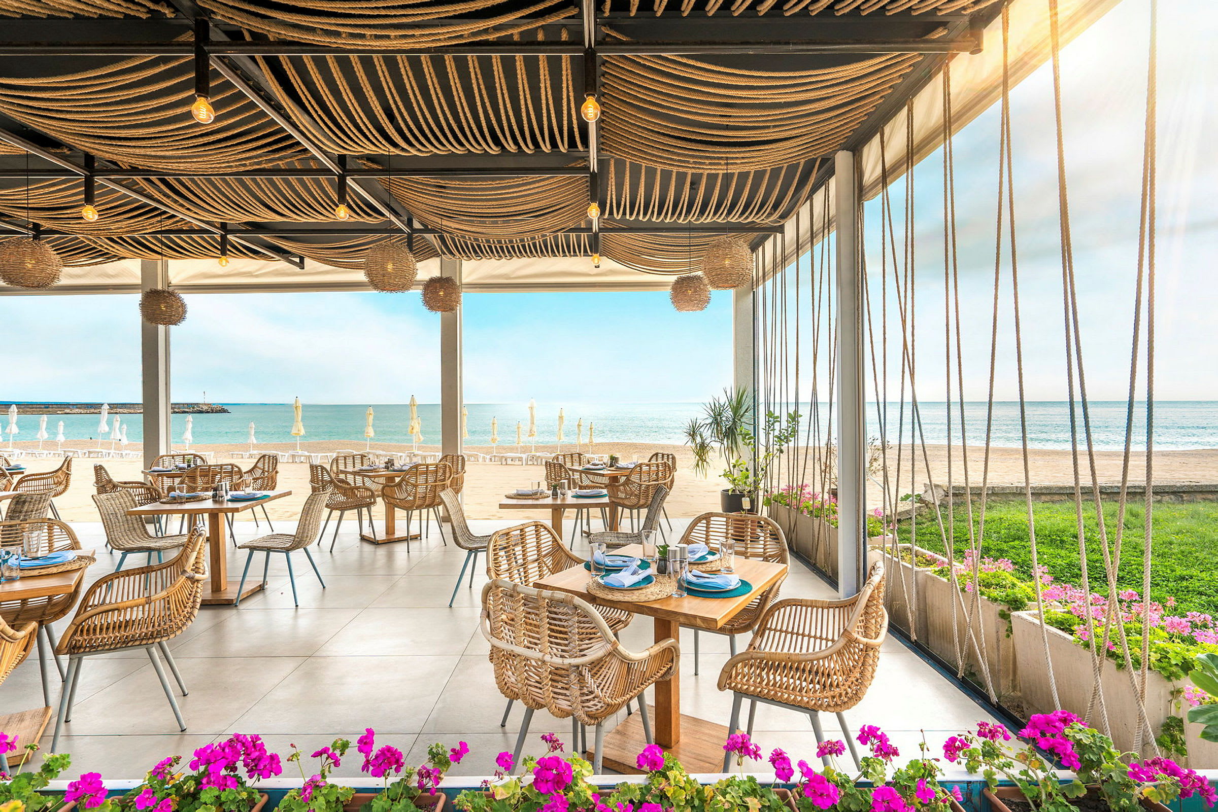 Restaurant ved stranden med utsikt over havet og bord med rottingstoler. (AI-generert tekst)