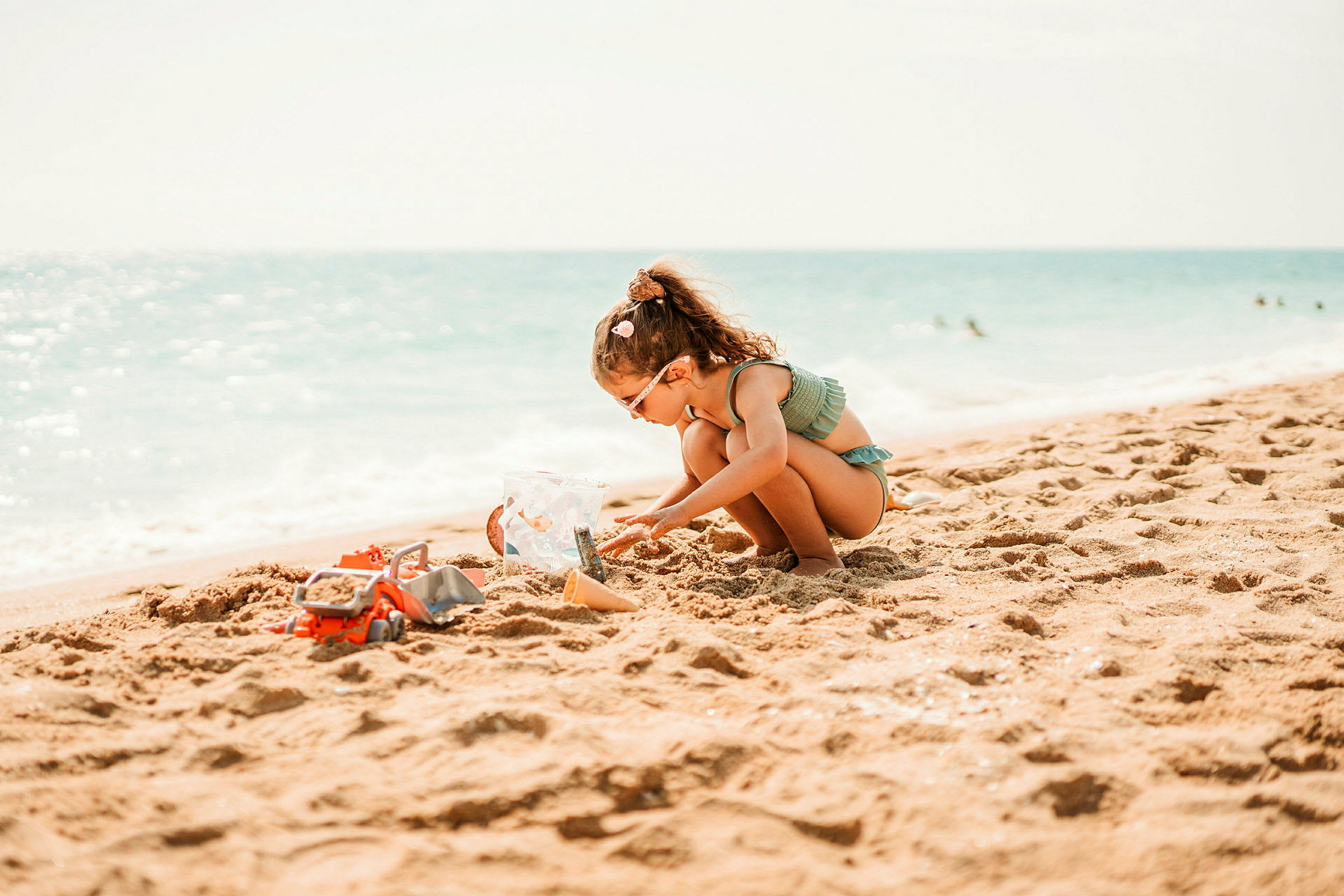 Et barn leker med sand og leker på en solrik strand nær havet. (AI-generert tekst)