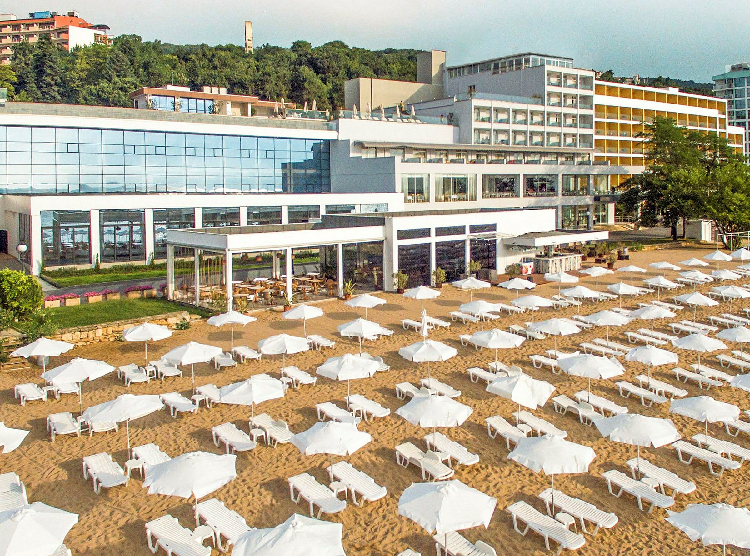 En strand med solsenger og parasoller foran et stort hotell. (AI-generert tekst)