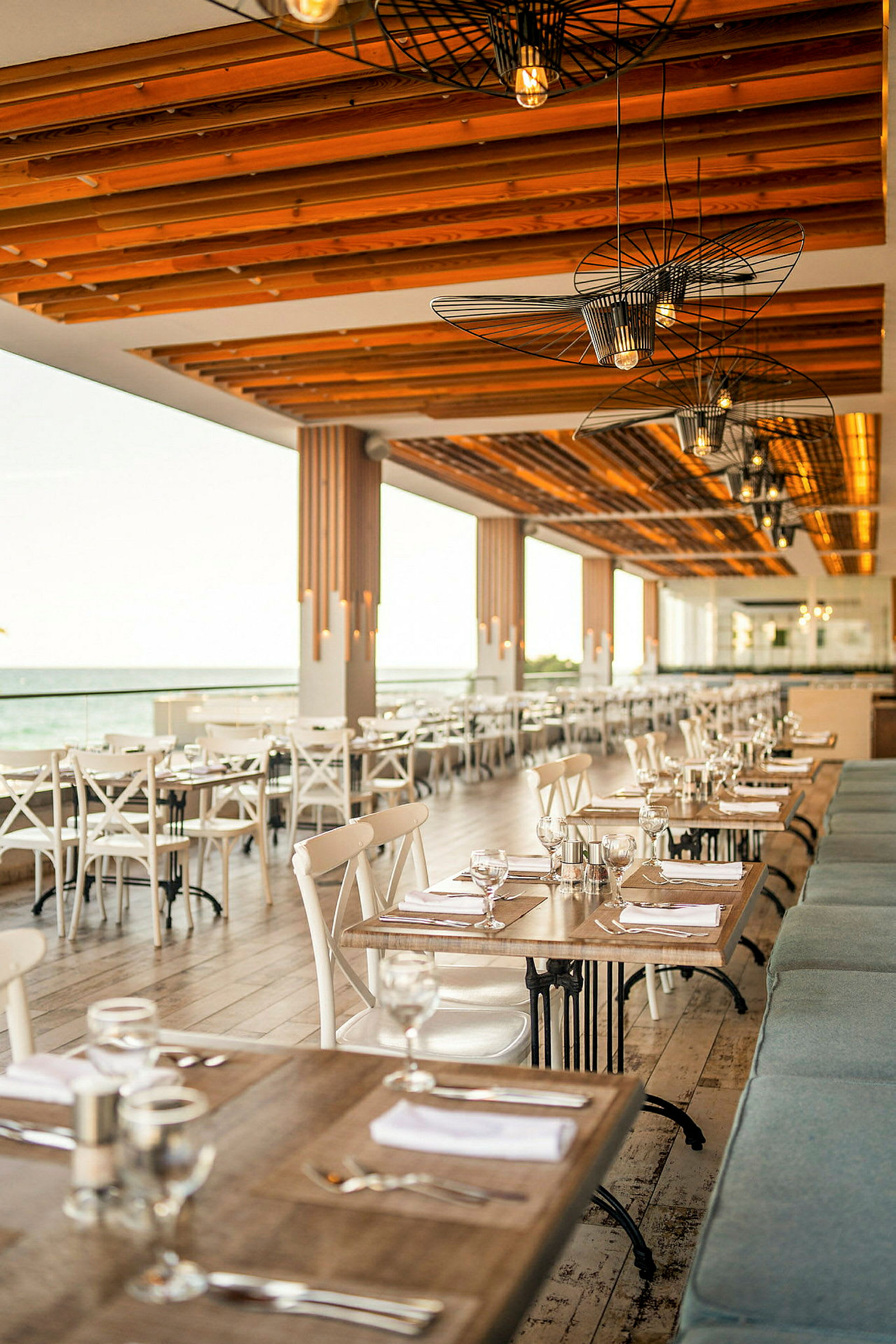 Restaurant med tre- og glassdesign med havutsikt. Bord er dekket med tallerkener og glass. (AI-generert tekst)