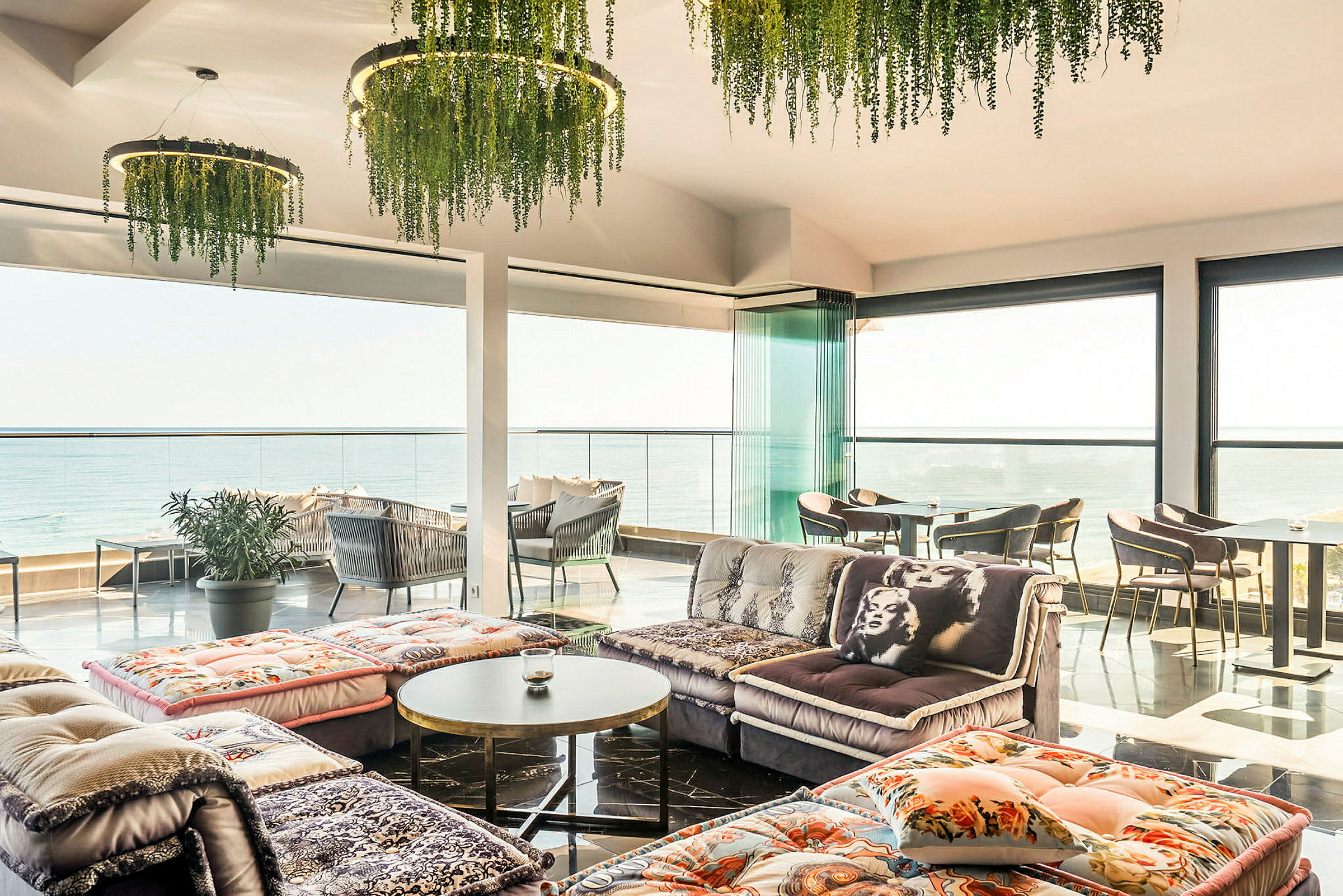 Et lyst innredet rom med panoramautsikt over havet, med sofaer og bord. (AI-generert tekst)