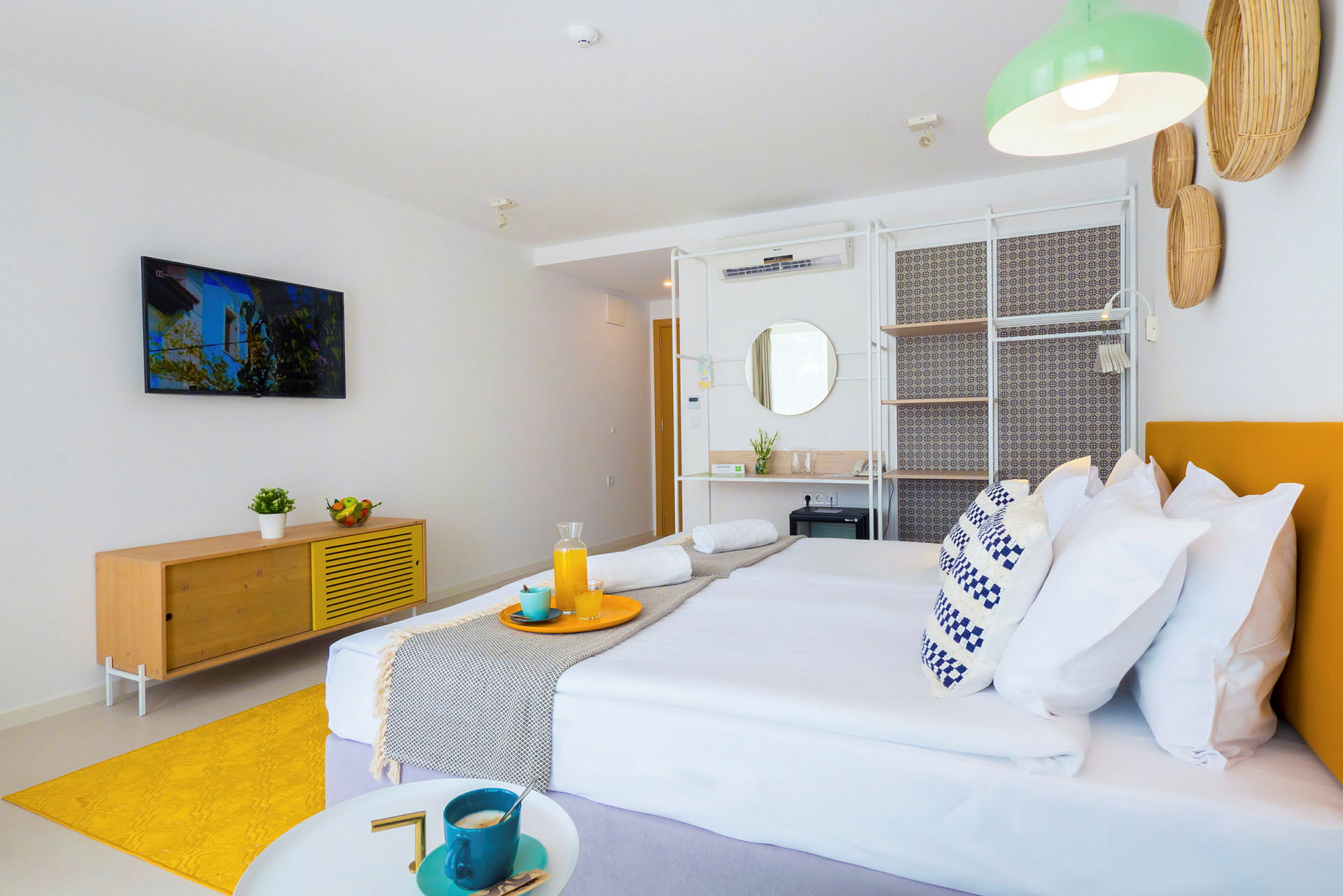 Et moderne og lyst hotellrom med en dobbeltseng, en TV montert på veggen og et gult teppe på gulvet. (AI-generert tekst)