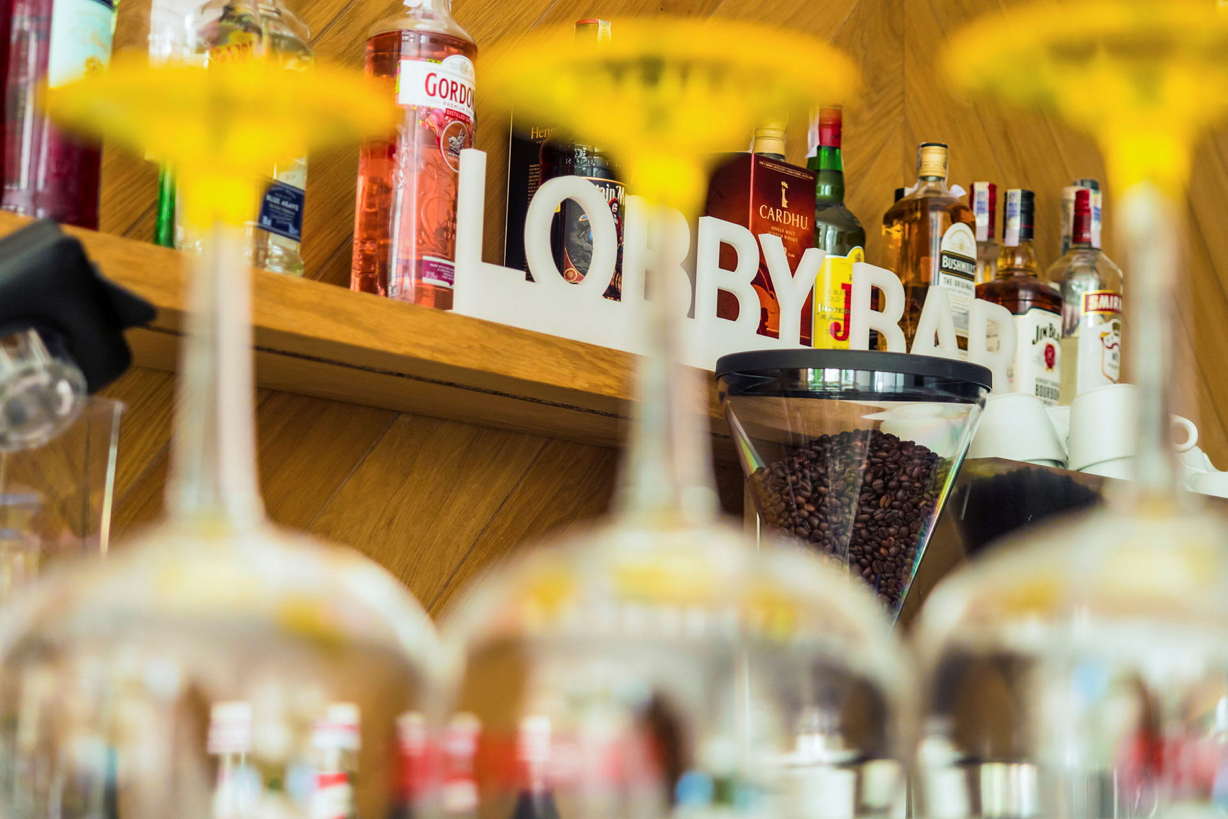 En hylle med flasker, kaffebønner og teksten 'LOBBY BAR' er synlig bak glass. (AI-generert tekst)