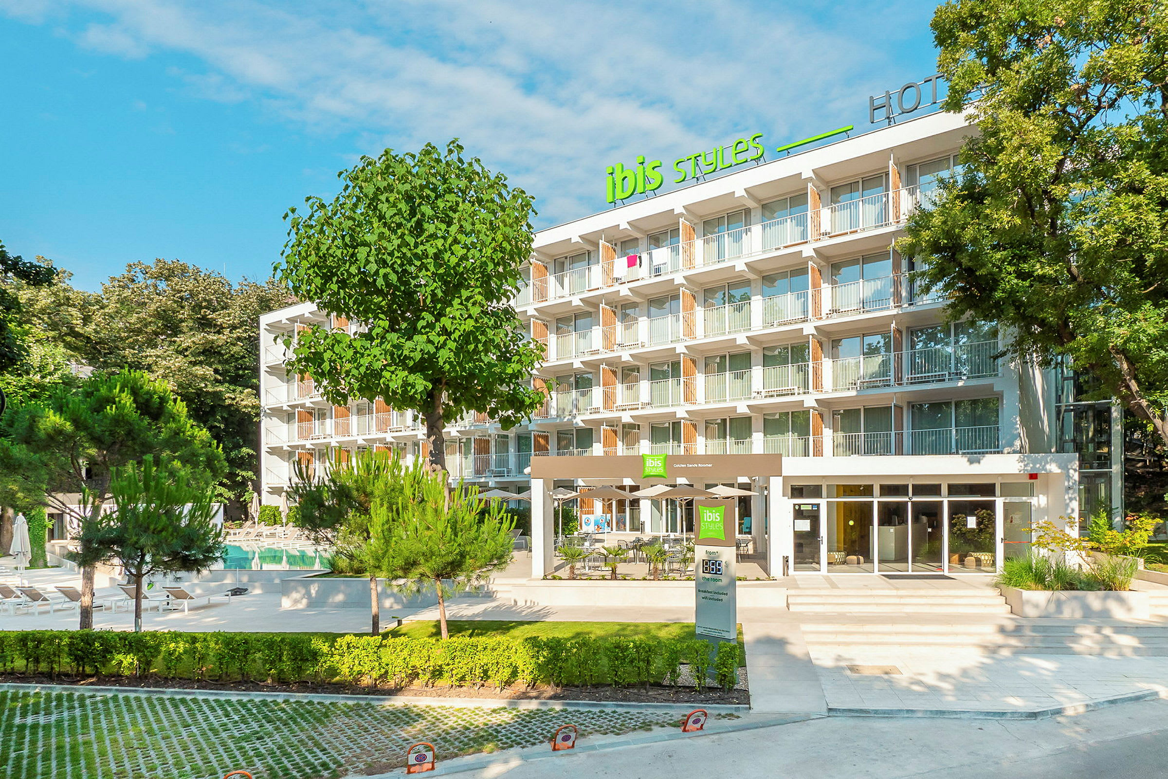 Hotellbygning med en moderne fasade og flere etasjer omgitt av grøntområder og trær. (AI-generert tekst)