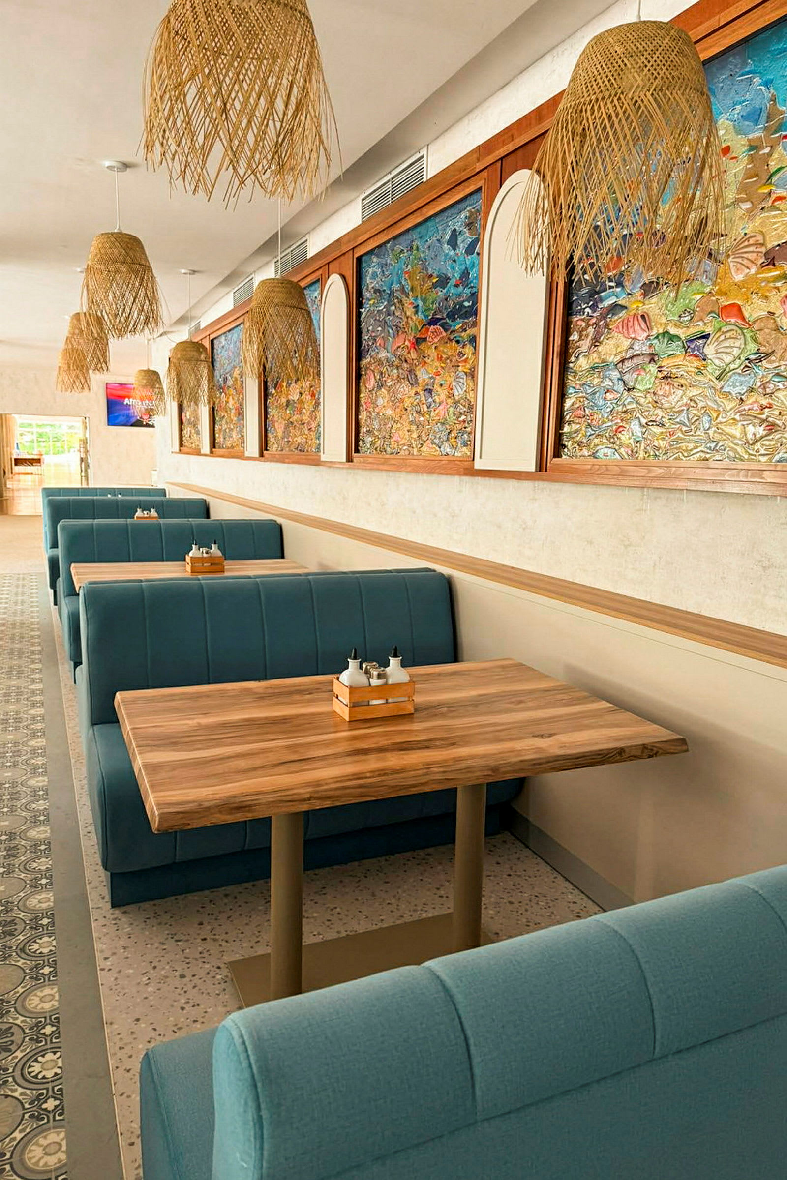 Bilde av en restaurant med blåe båser og trebord. Veggene er dekorert med fargerike kunstverk og taket har flettede lamper. (AI-generert tekst)