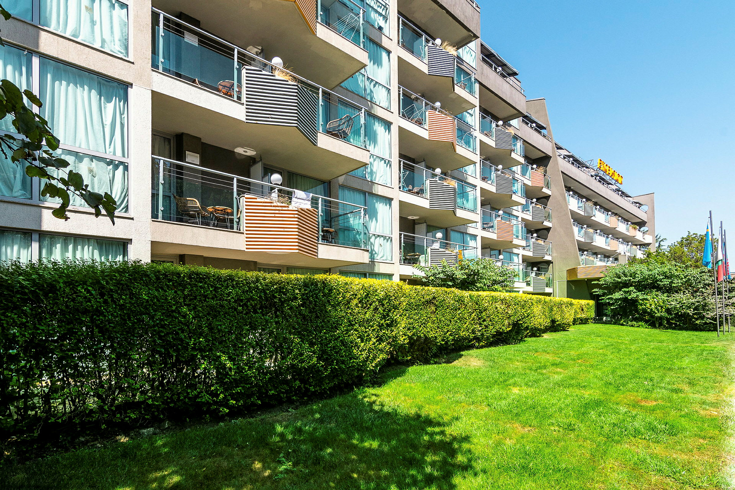 Bilde av en hotellbygning med flere balkonger og omkringliggende grøntområder. (AI-generert tekst)