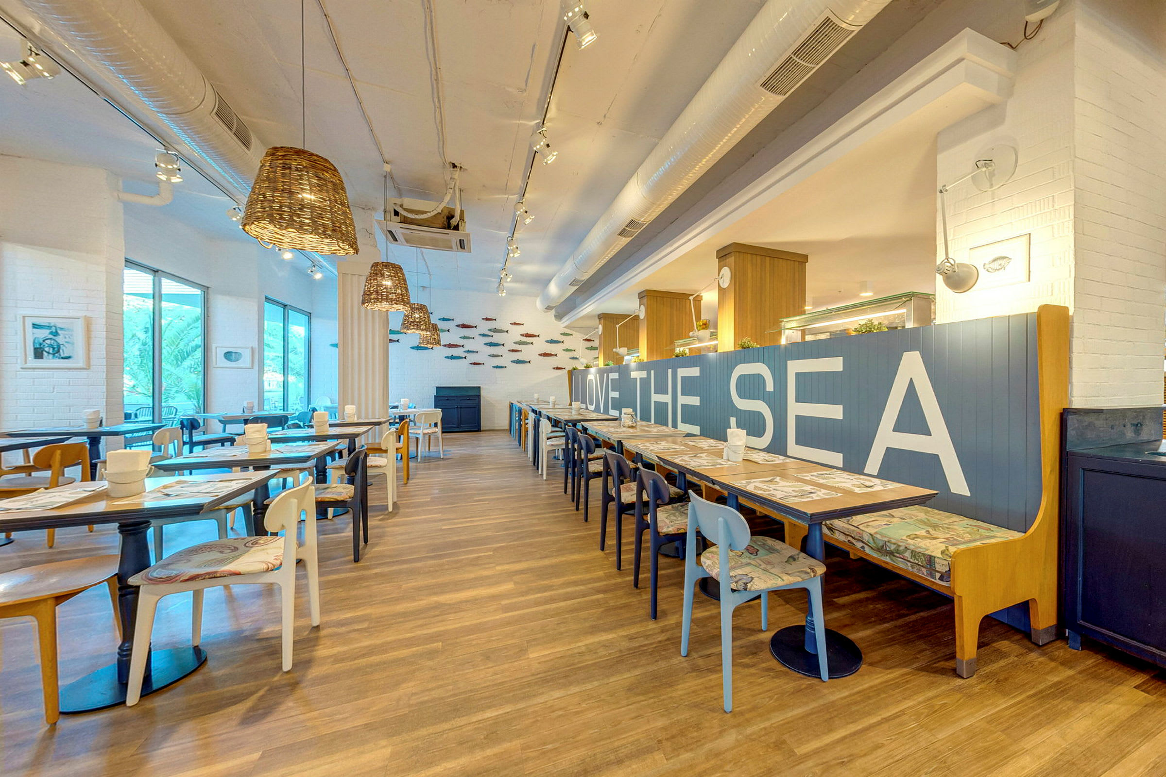 En moderne restaurant med lys innredning, trebord og stoler, samt teksten 'LOVE THE SEA' på en blå ryggstøtte. (AI-generert tekst)