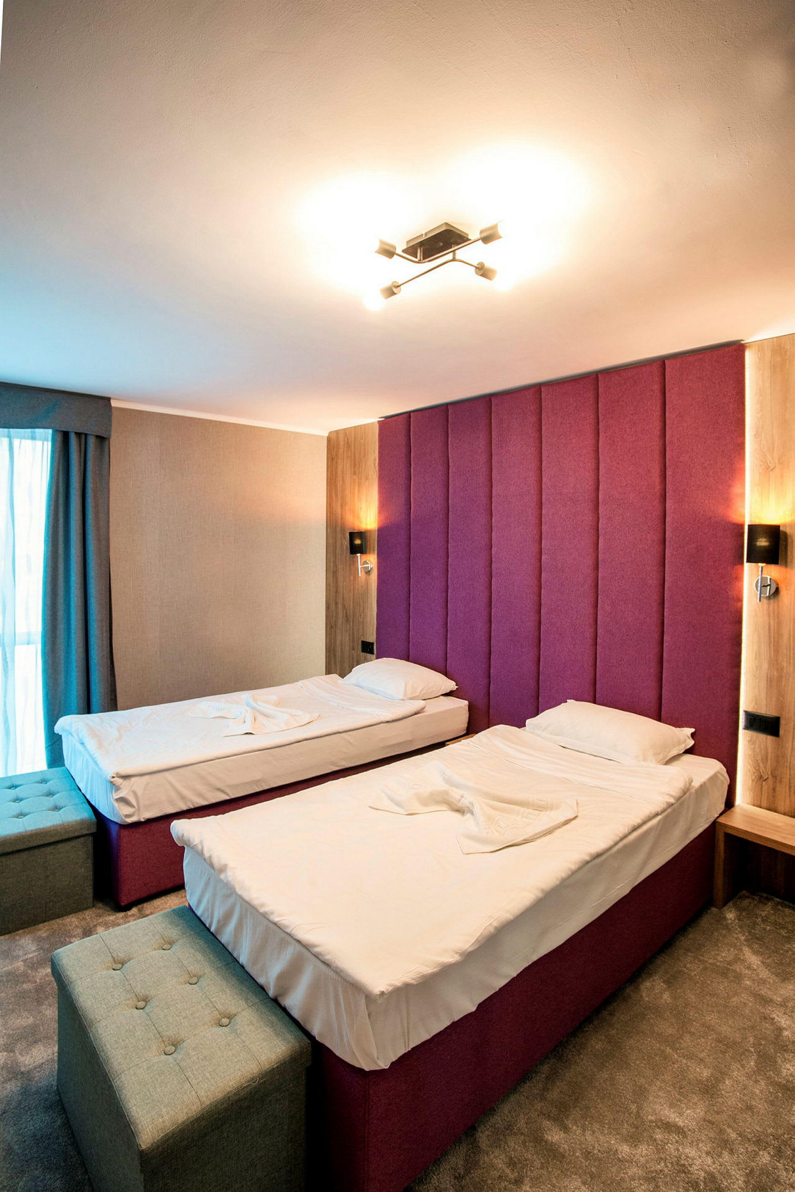 Et hotellrom med to enkeltsenger, en lilla hodegjerde og interiør i moderne stil. (AI-generert tekst)