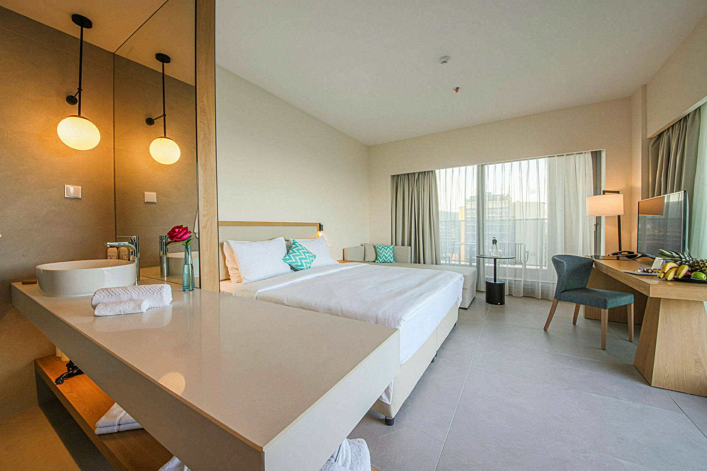 Et hotellrom med en dobbeltseng, et skrivebord med stol og et stort speil ved vasken. (AI-generert tekst)