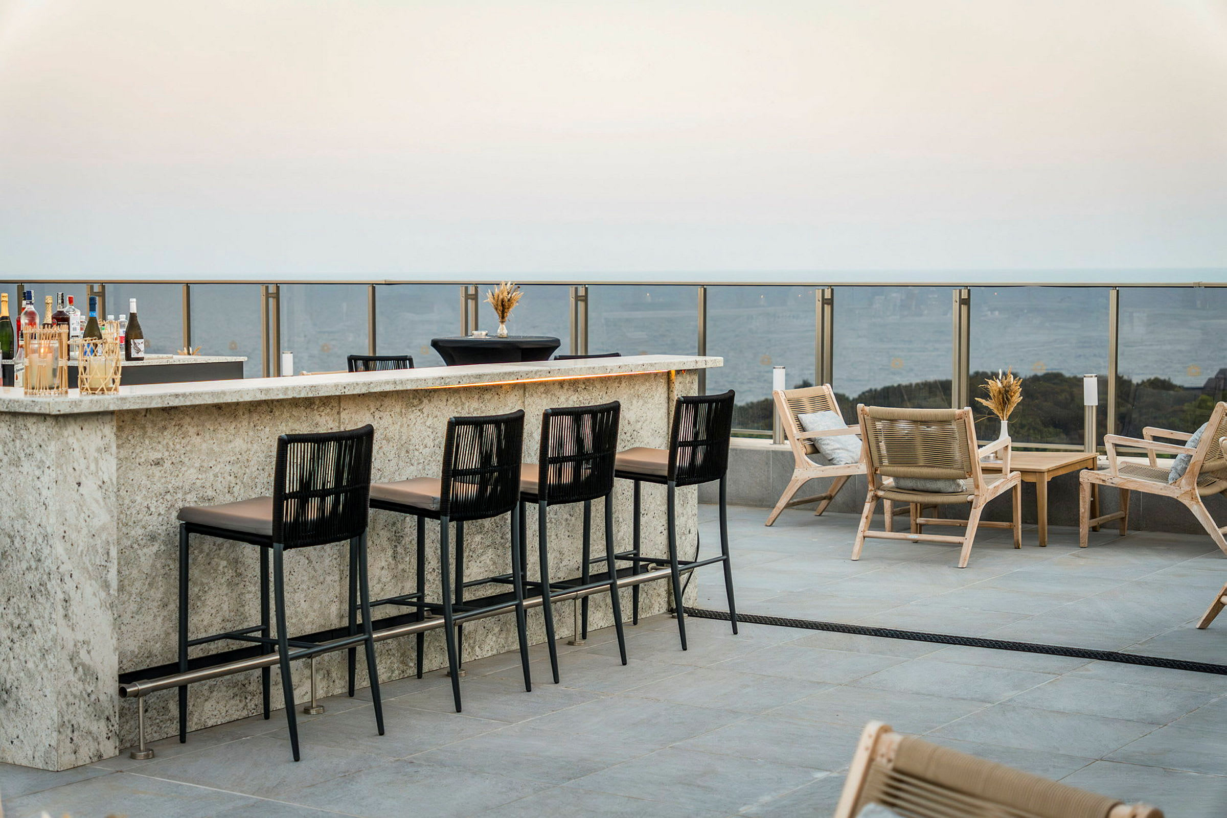 En utendørsbar med høye stoler og loungemøbler på en terrasse med utsikt. (AI-generert tekst)