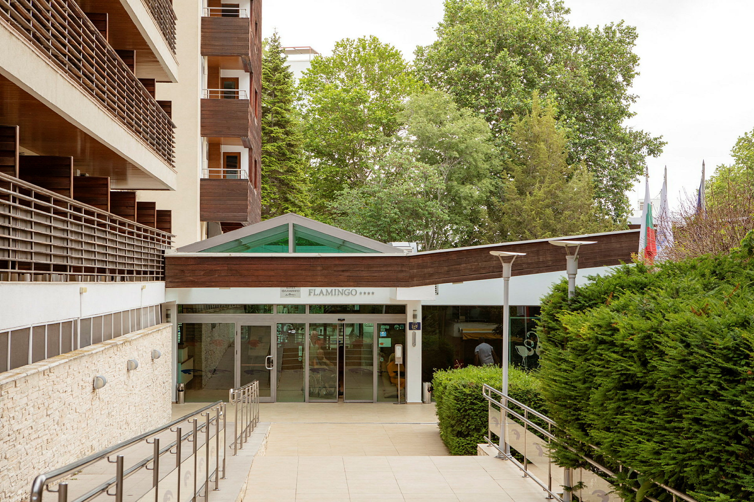 Hotellinngang med glassdører og omkringliggende grøntområde. (AI-generert tekst)