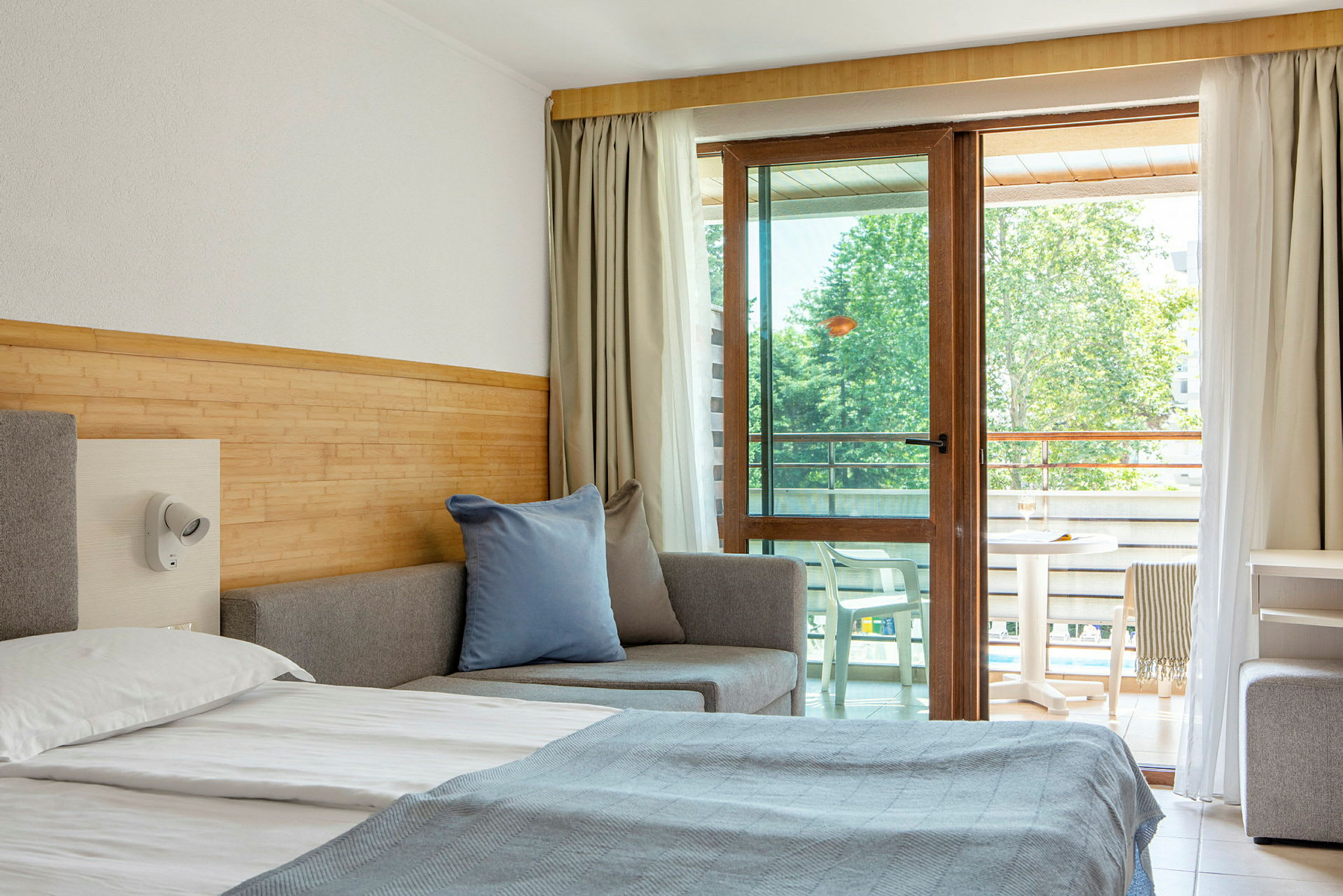 Et hotellrom med en seng, sofa og balkongmøbler synlige gjennom en glassdør. (AI-generert tekst)