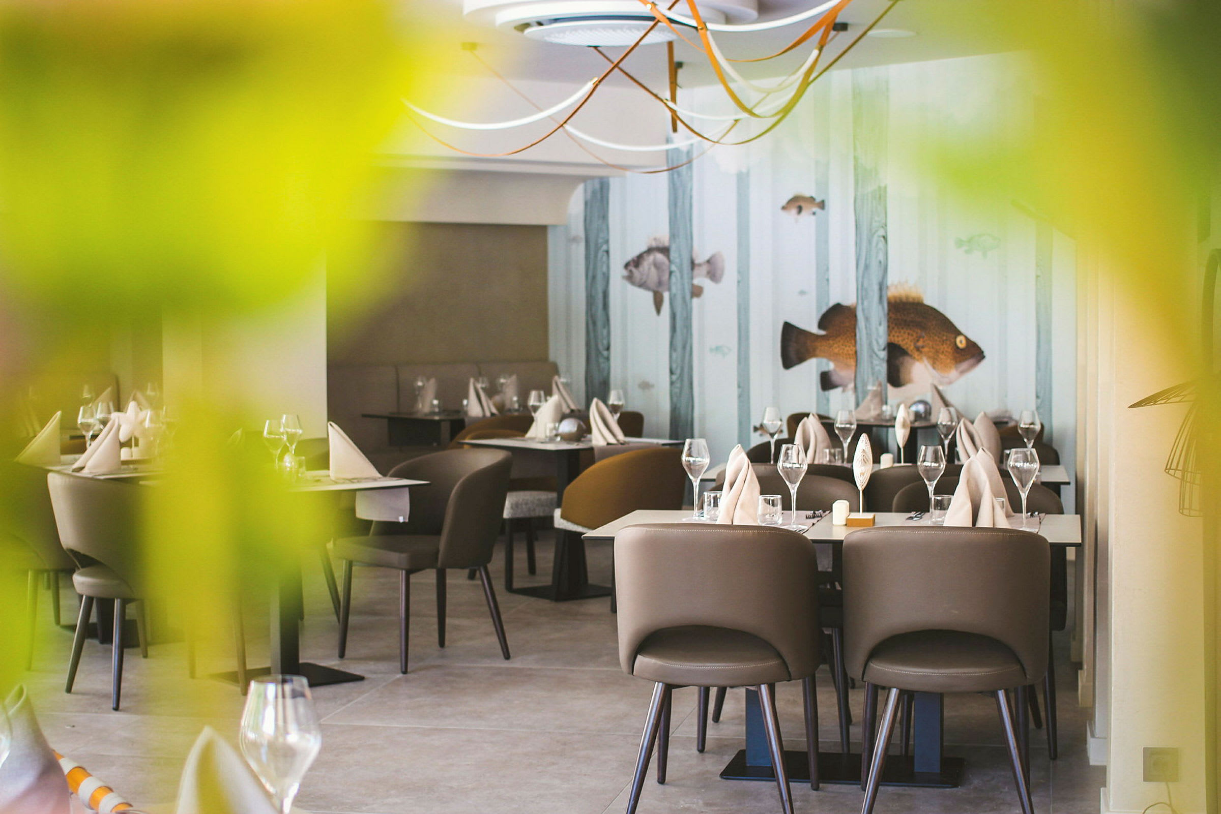 Restaurant med dekkede bord, brune stoler og dekorasjoner med fiskemotiv på veggen. (AI-generert tekst)
