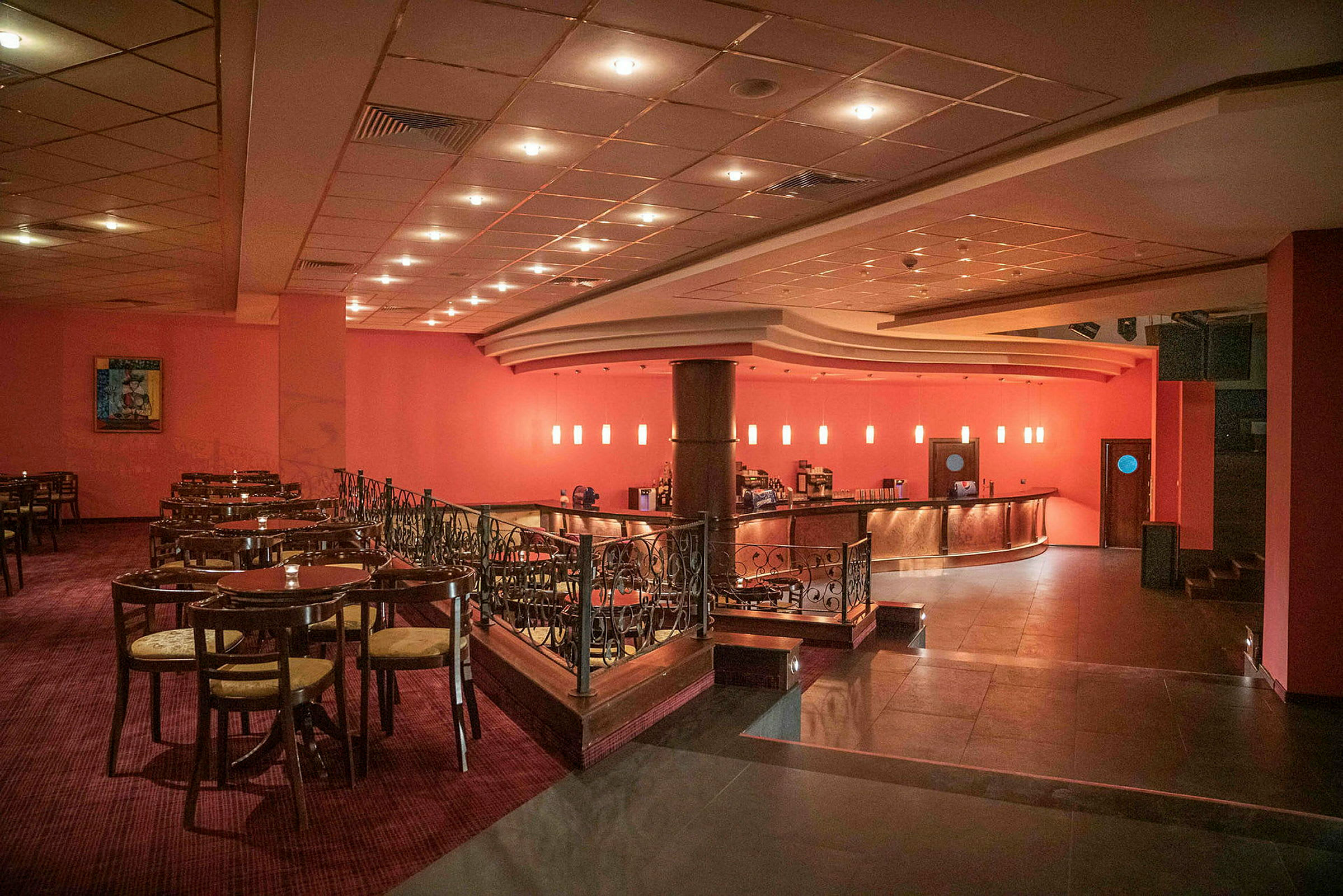 En restaurant med bord og stoler samt en bar med glødende lamper i bakgrunnen. (AI-generert tekst)