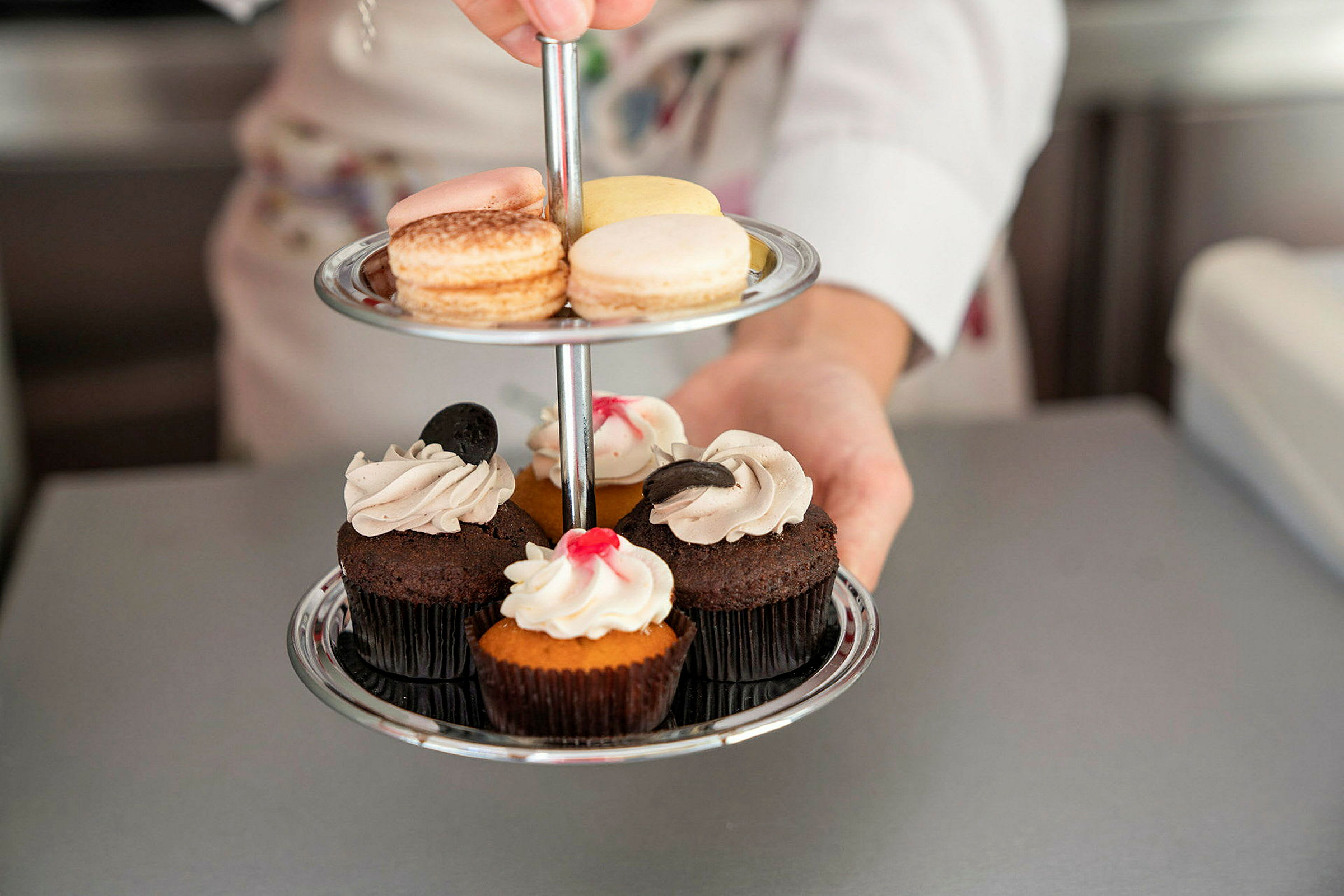 En person holder et toetasjes serveringsfat med makarons og muffins. (AI-generert tekst)