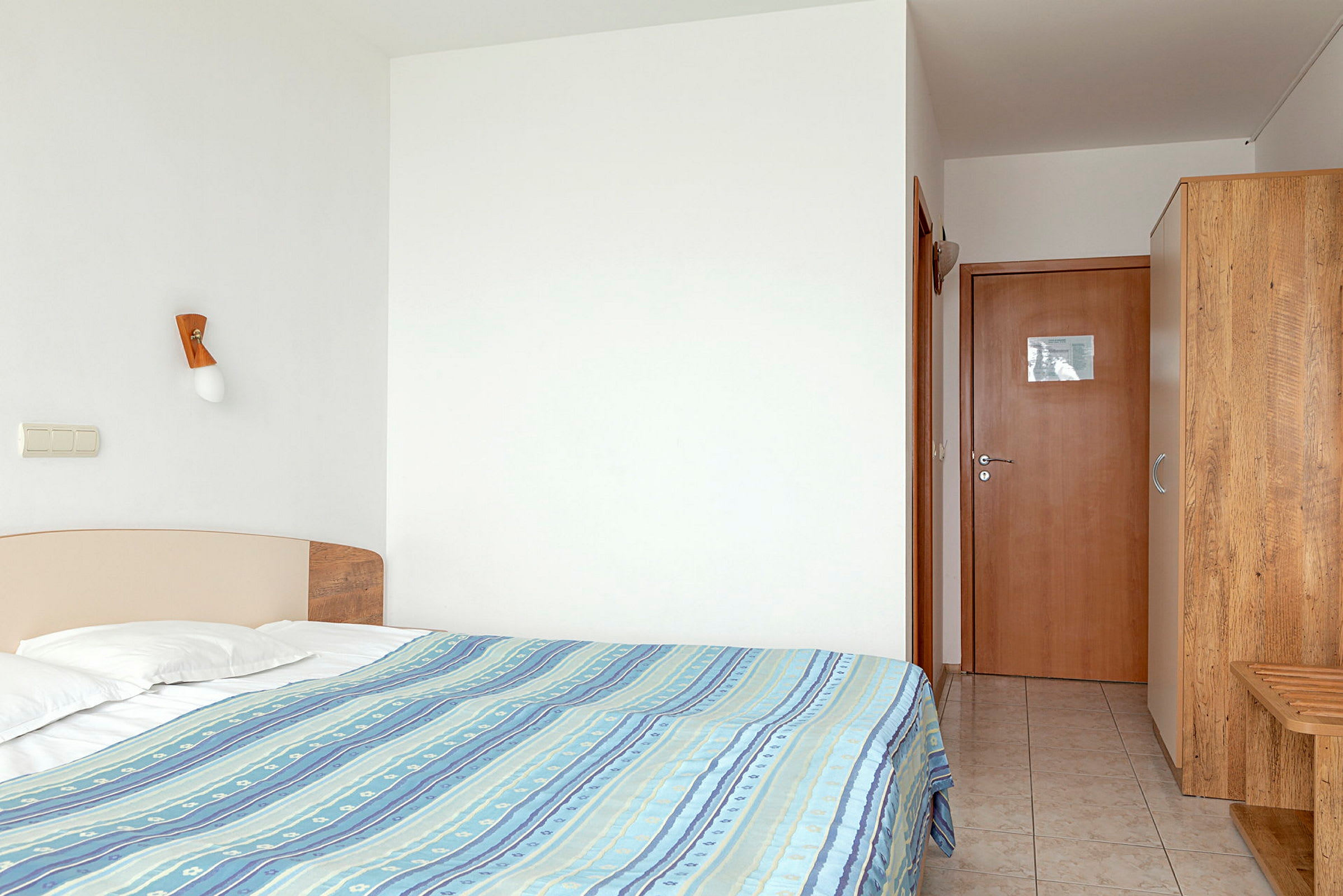 Hotellrom med seng, garderob og døråpning. (AI-generert tekst)