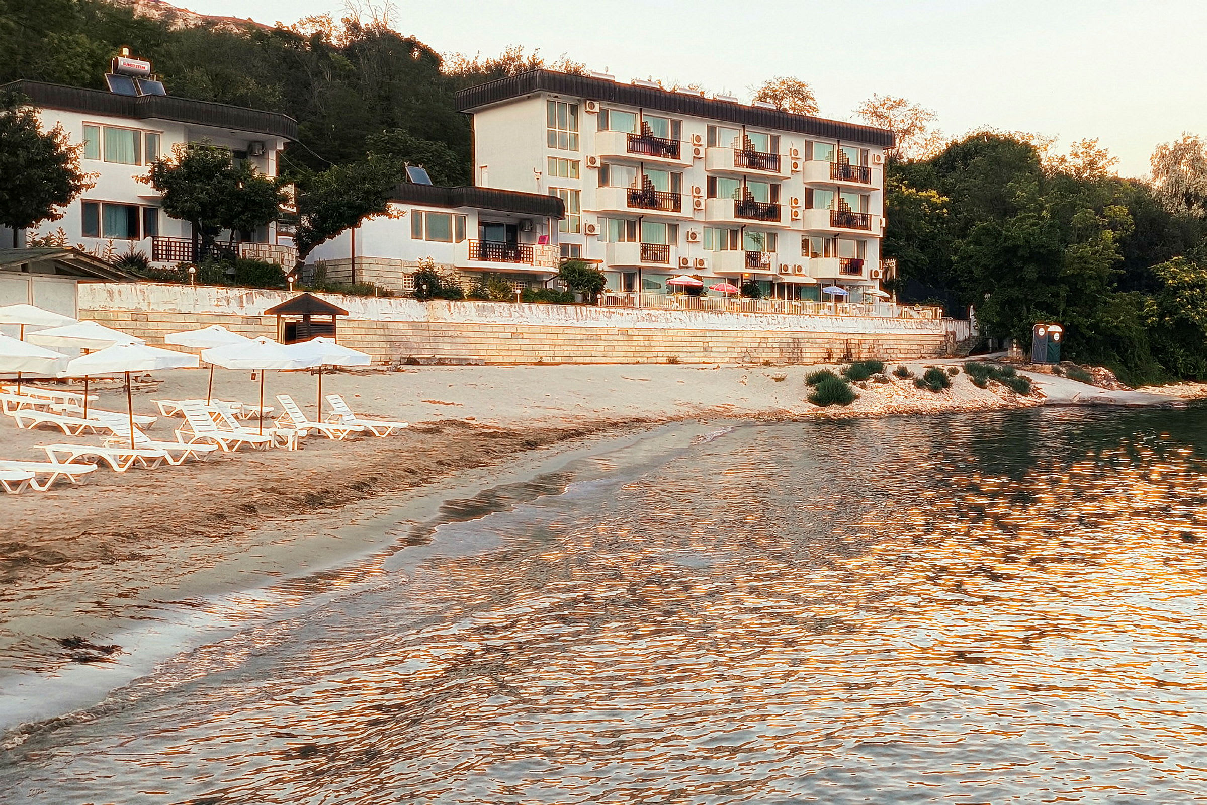 Strand med solsenger og parasoller foran en hvit bygning. (AI-generert tekst)
