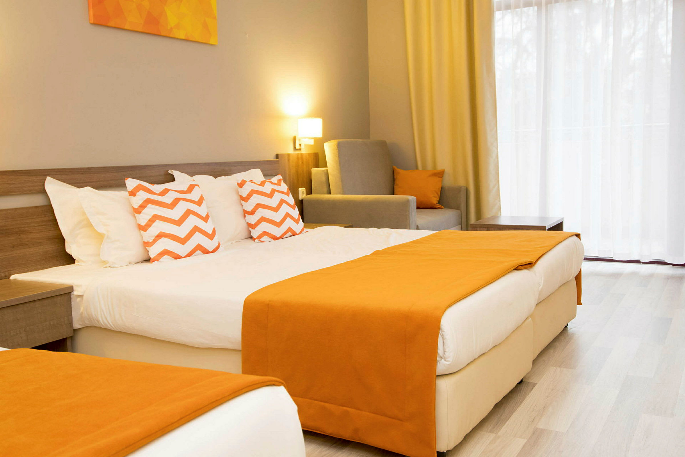 Hotellrom med en dobbeltseng dekorert med oransje tepper og puter med sikksakkmønster. (AI-generert tekst)