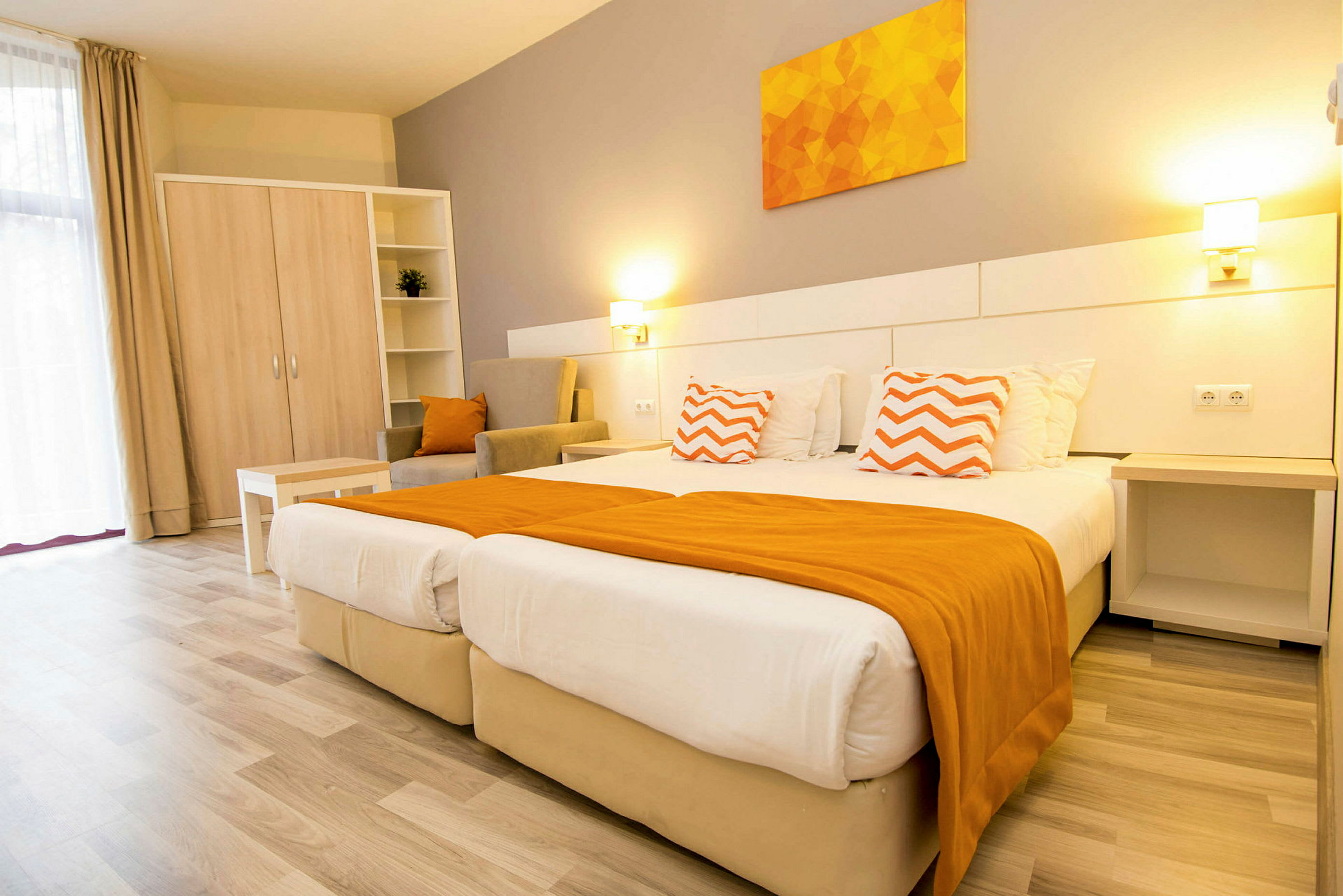 Et lyst hotellrom med to senger, orange detaljer og møbler. (AI-generert tekst)