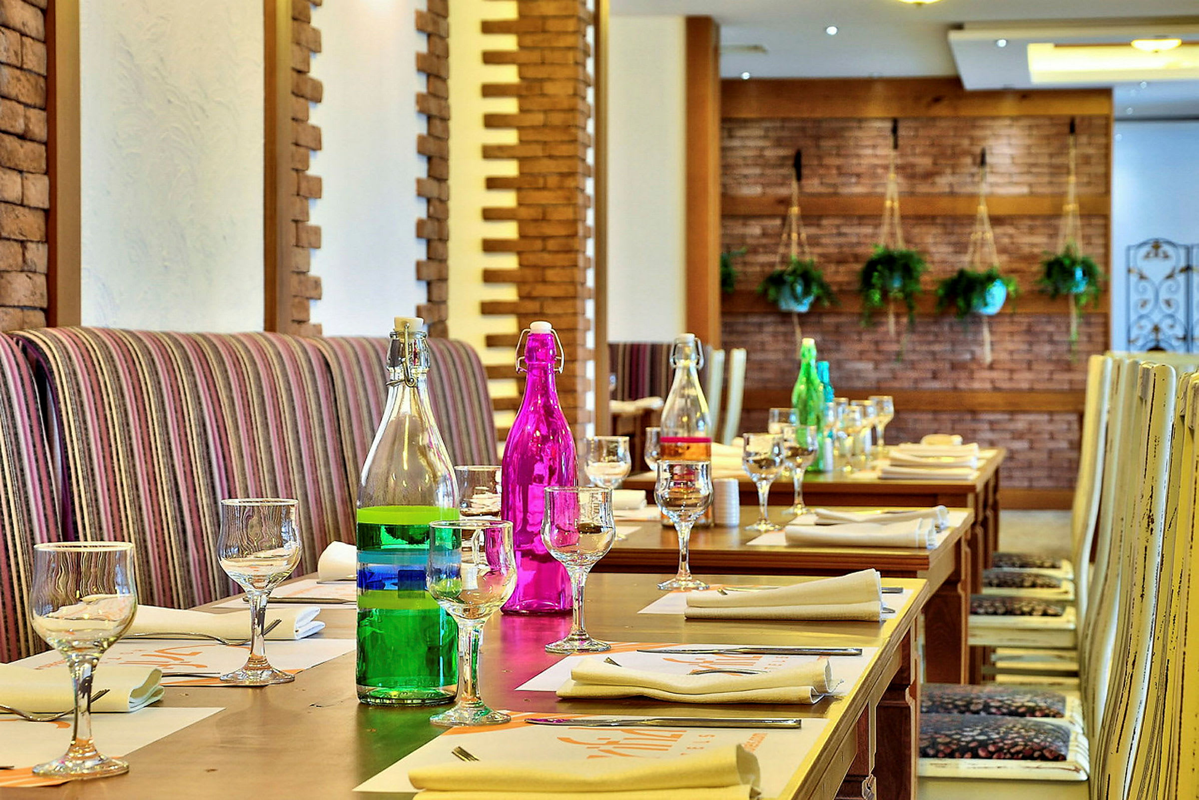 Et innendørsbord dekket med glass og fargerike flasker i en restaurant med veggdekorasjoner. (AI-generert tekst)