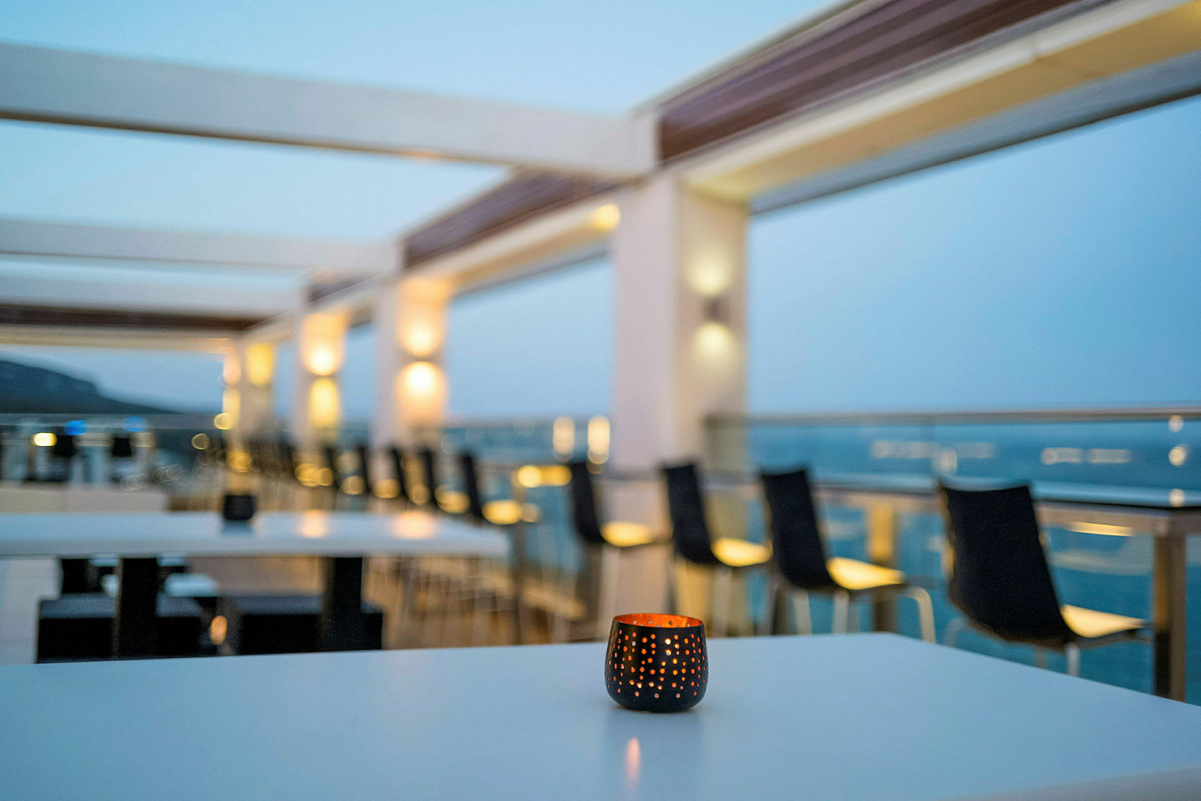 Utsikt over en terrasse med bord og stoler, med et lys foran. (AI-generert tekst)