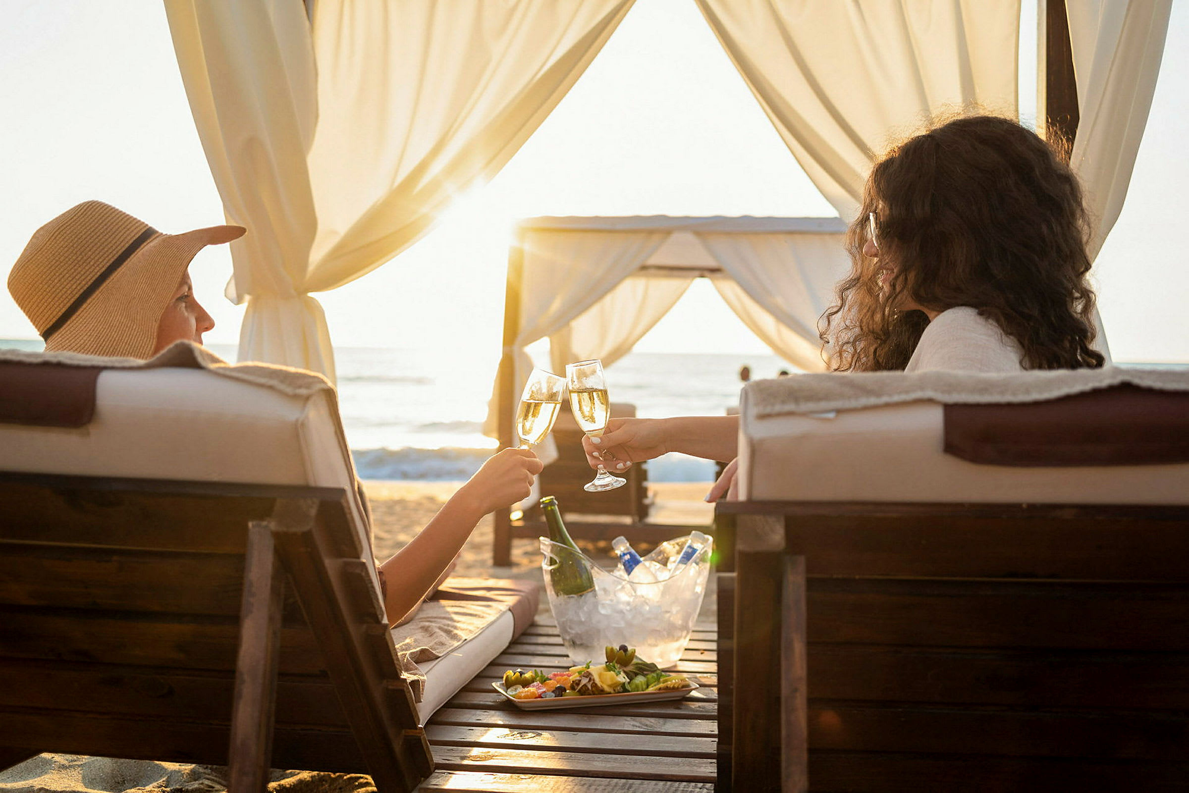 To personer skåler med glass på en strand under en baldakin. (AI-generert tekst)