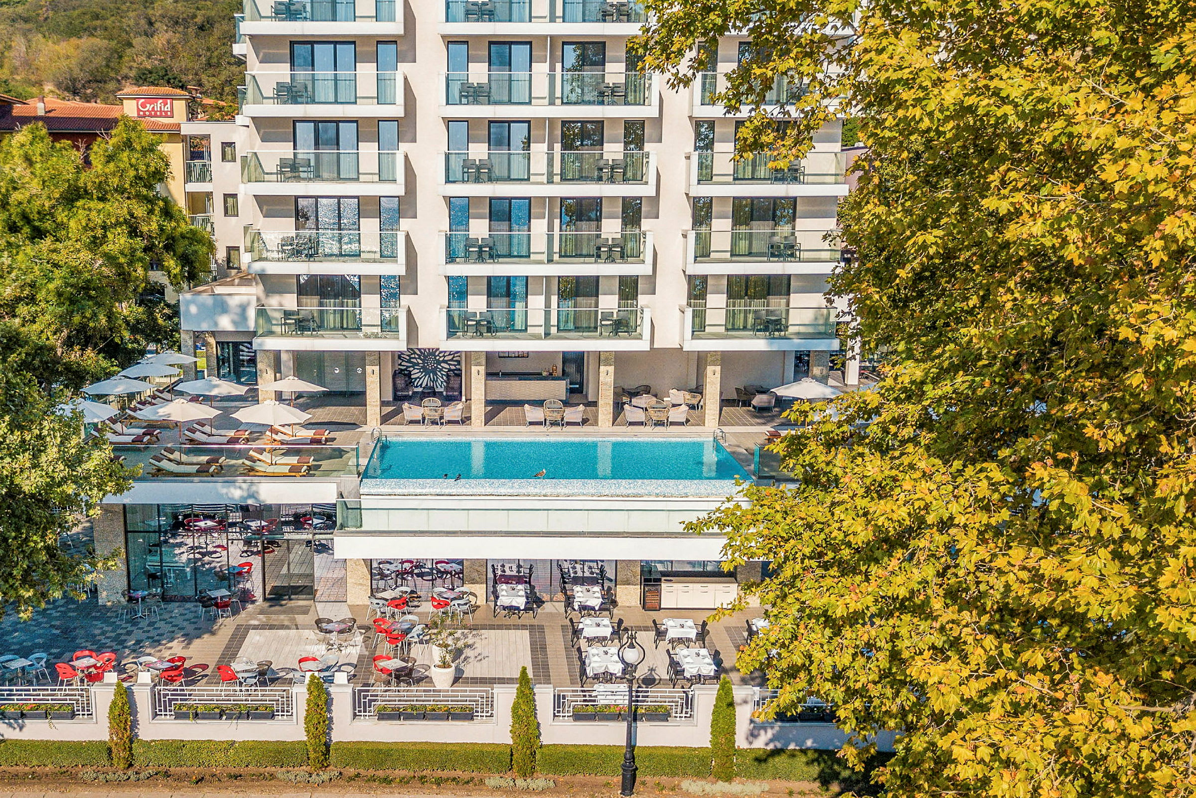 Hotell med balkonger, basseng og uteservering omgitt av grøntområder. (AI-generert tekst)