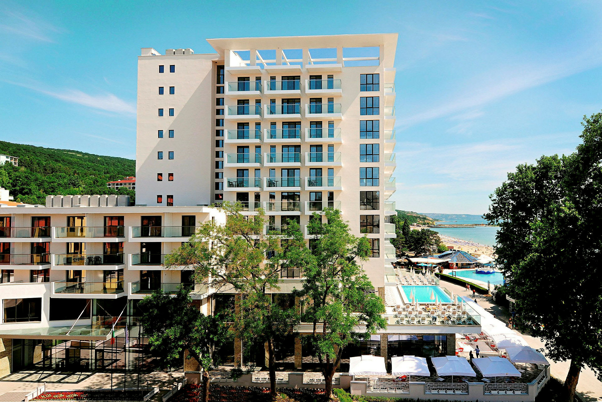 Bilde av en moderne hotellbygning med et basseng i sitt område, beliggende ved havet. (AI-generert tekst)
